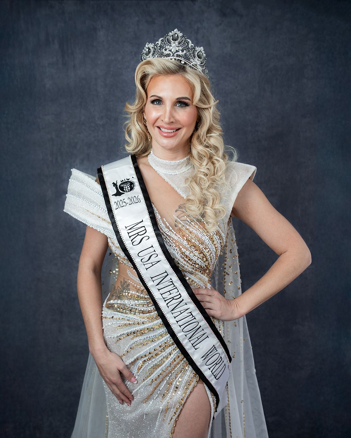 Beauty pageant winner poses in sparkling gown and crown against dark backdrop.