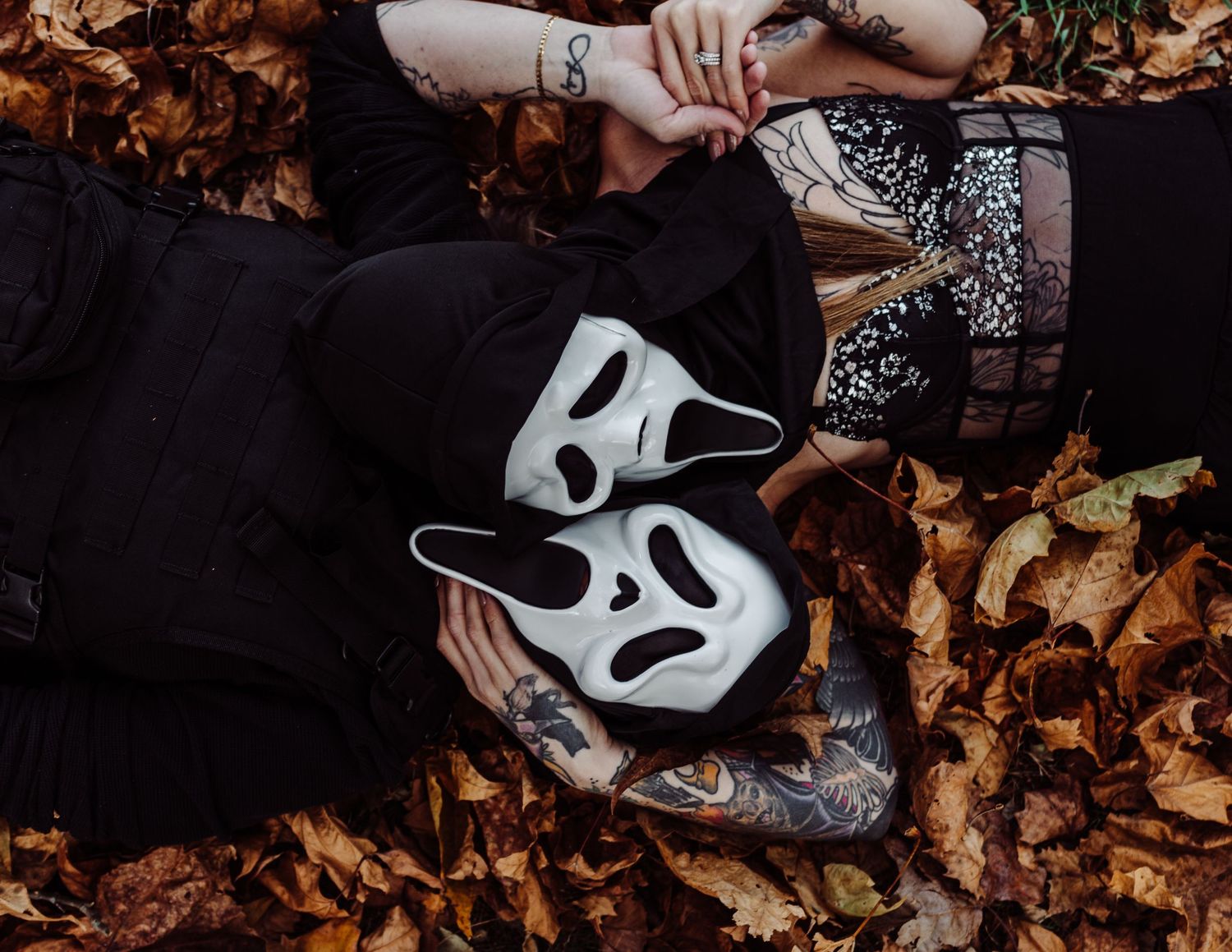 A person wearing a ghostface mask poses dramatically against autumn leaves.