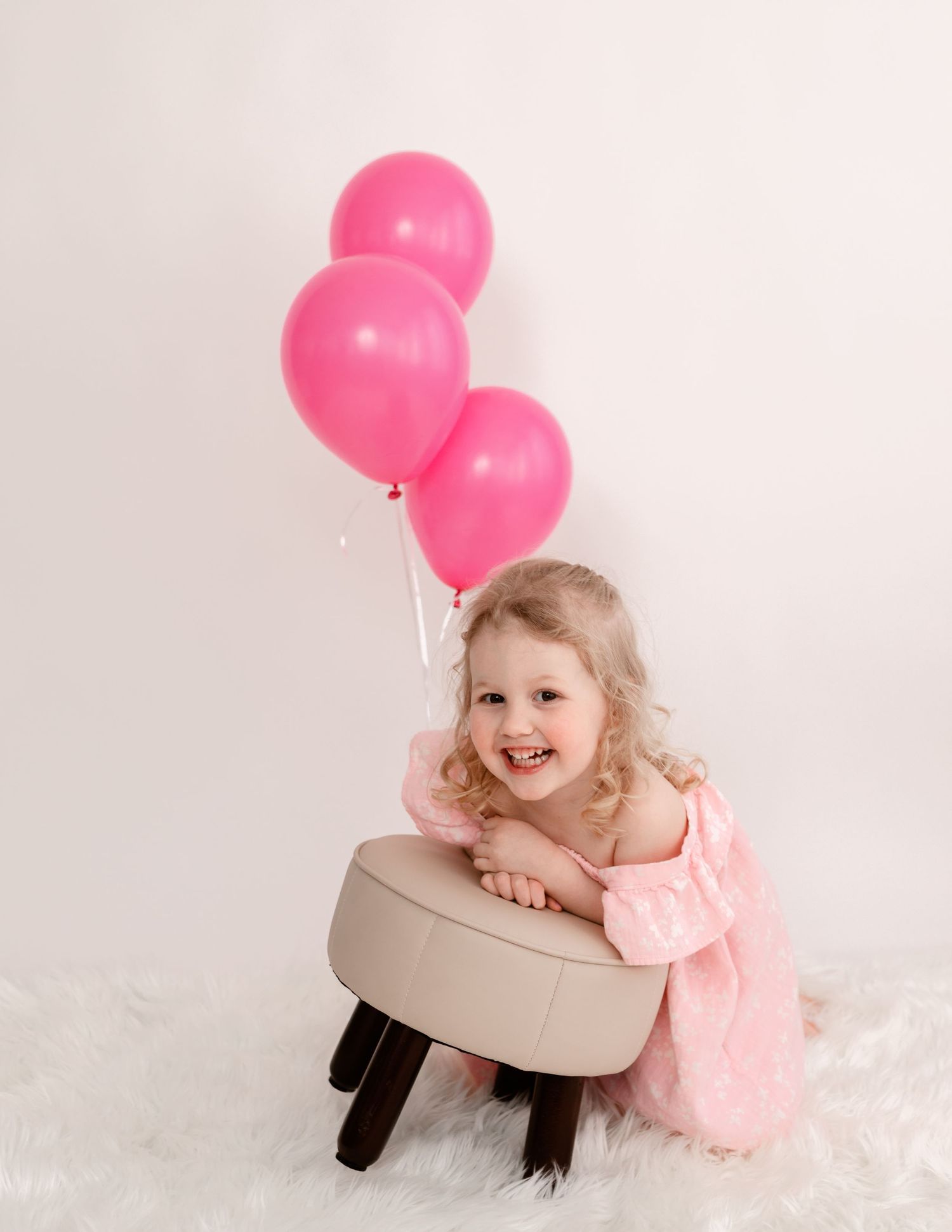 Child in pink dress poses with pink balloons against white backdrop in four sequential playful photos.