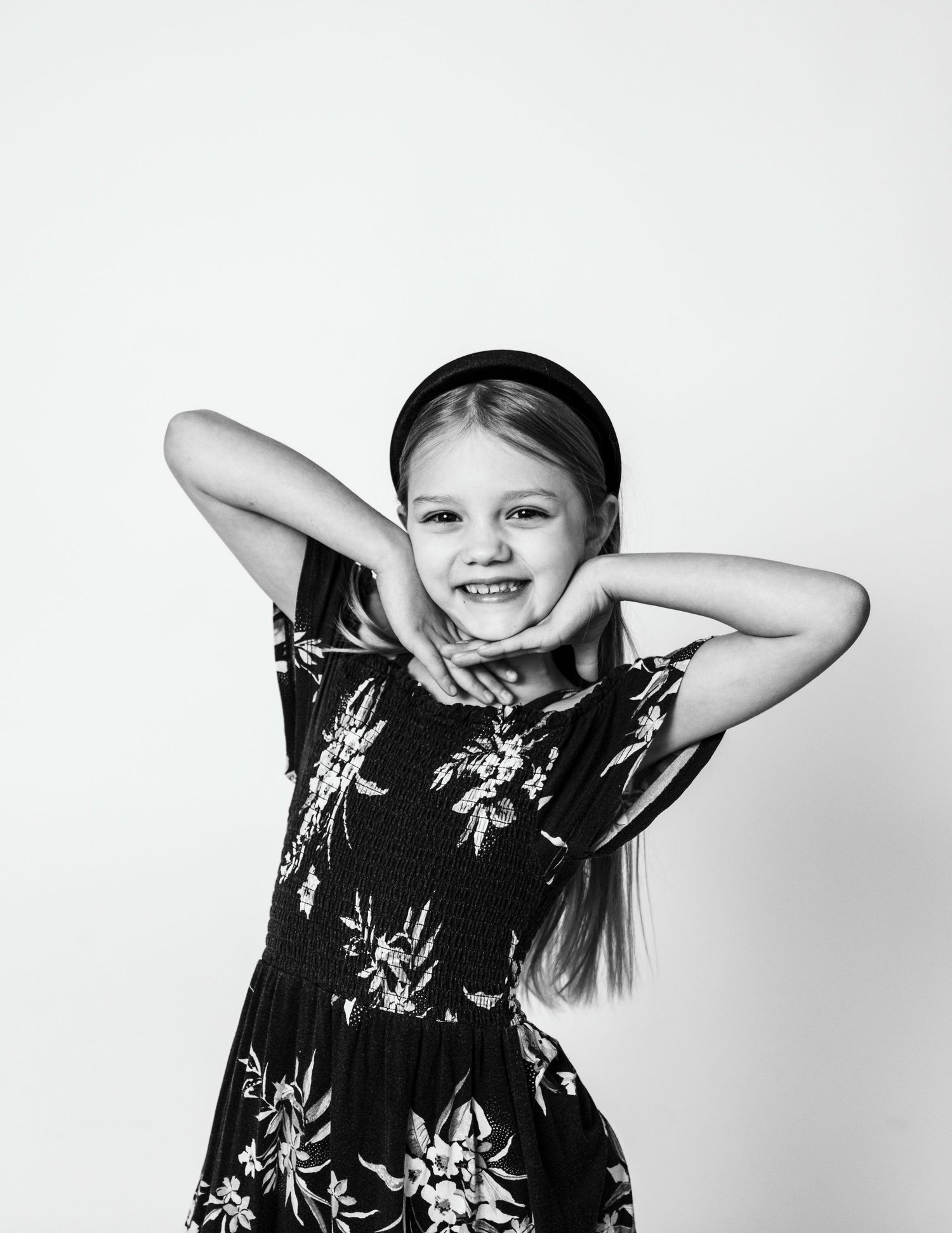 A cheerful black and white portrait with hands behind head in a floral dress.