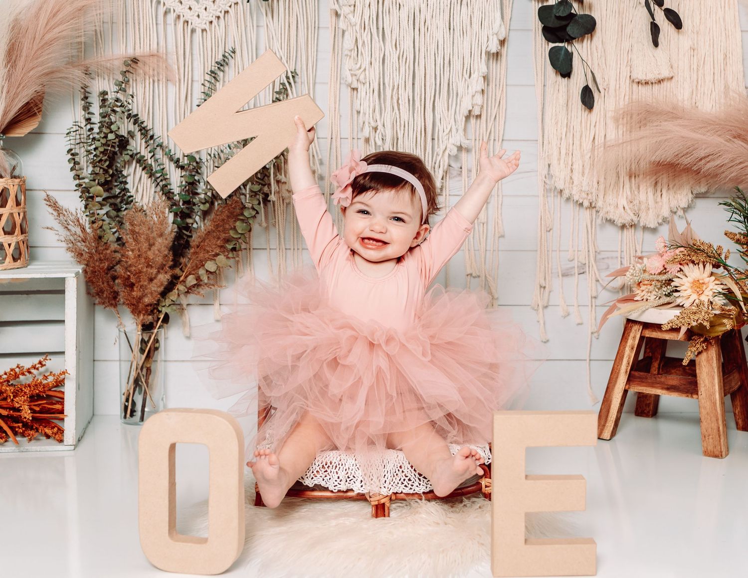Baby girl in pink tutu dress playing with birthday decorations in boho-themed photoshoot.