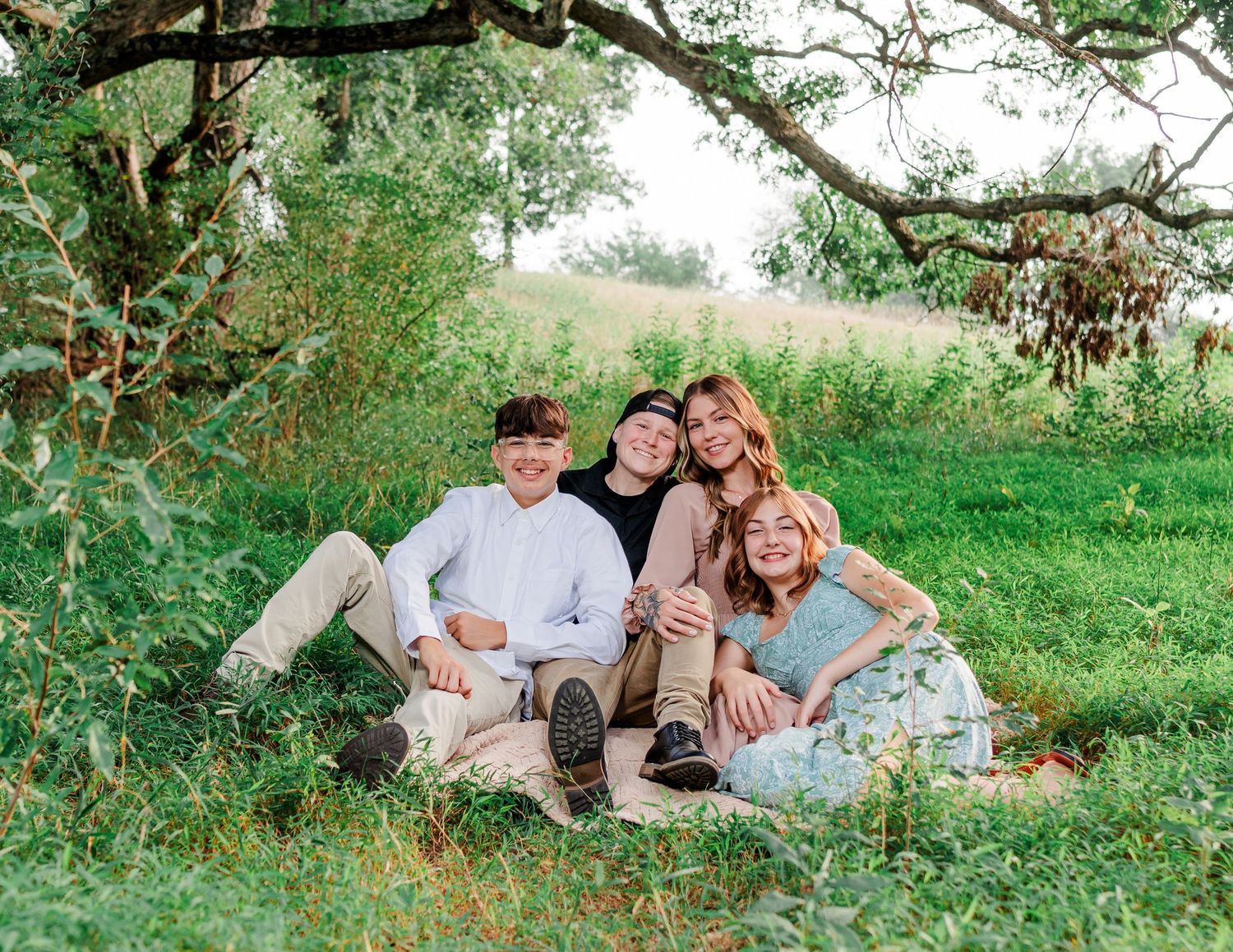 Family relaxing together under a tree branch in a scenic outdoor setting.