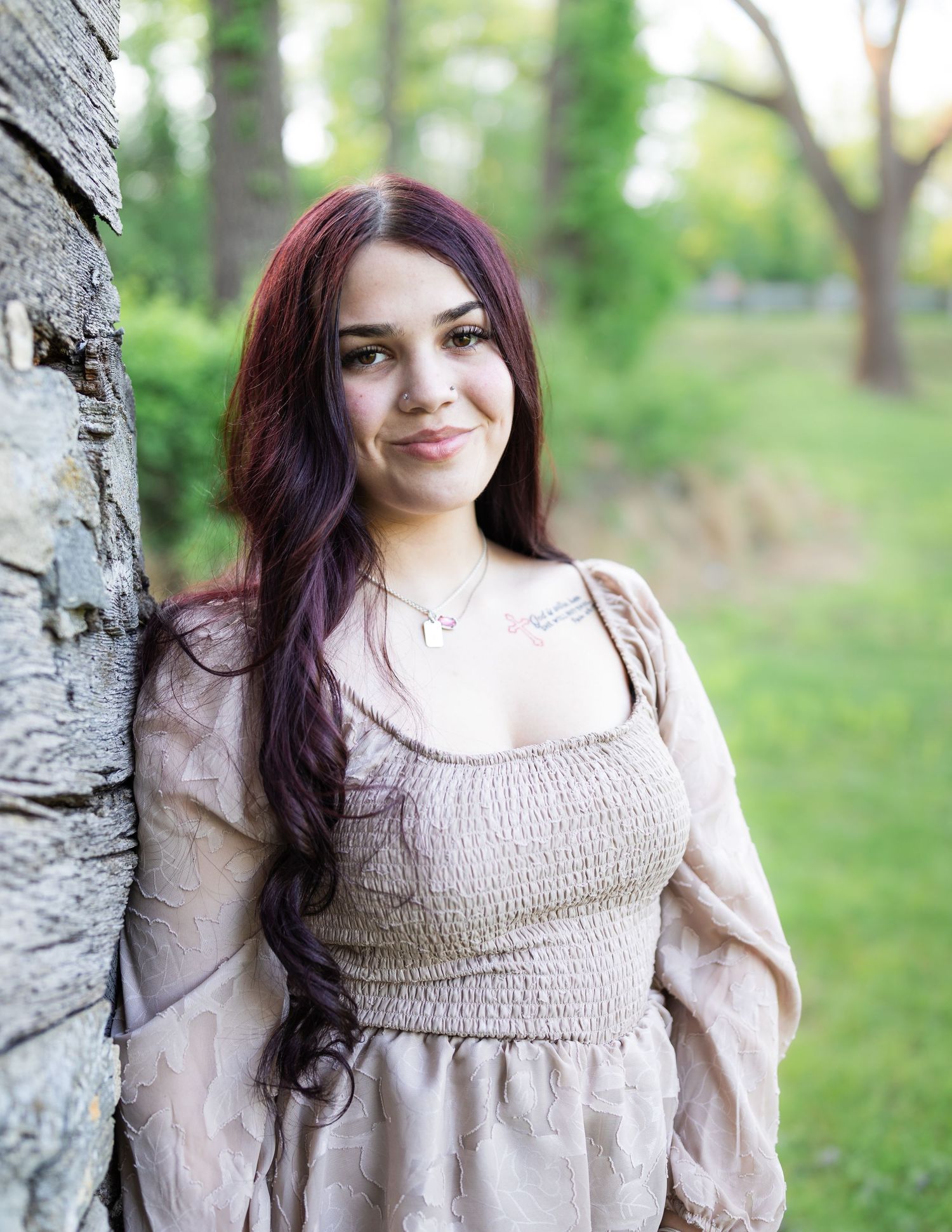 Woman in vintage-style beige smocked dress poses in outdoor garden setting with soft natural lighting.