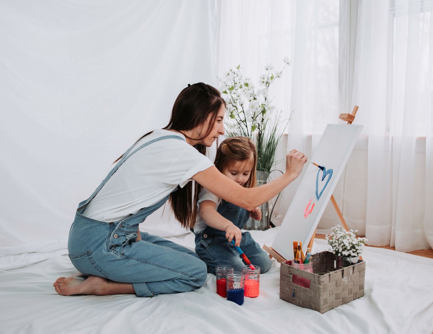 Parent and child exploring art supplies together on white backdrop.