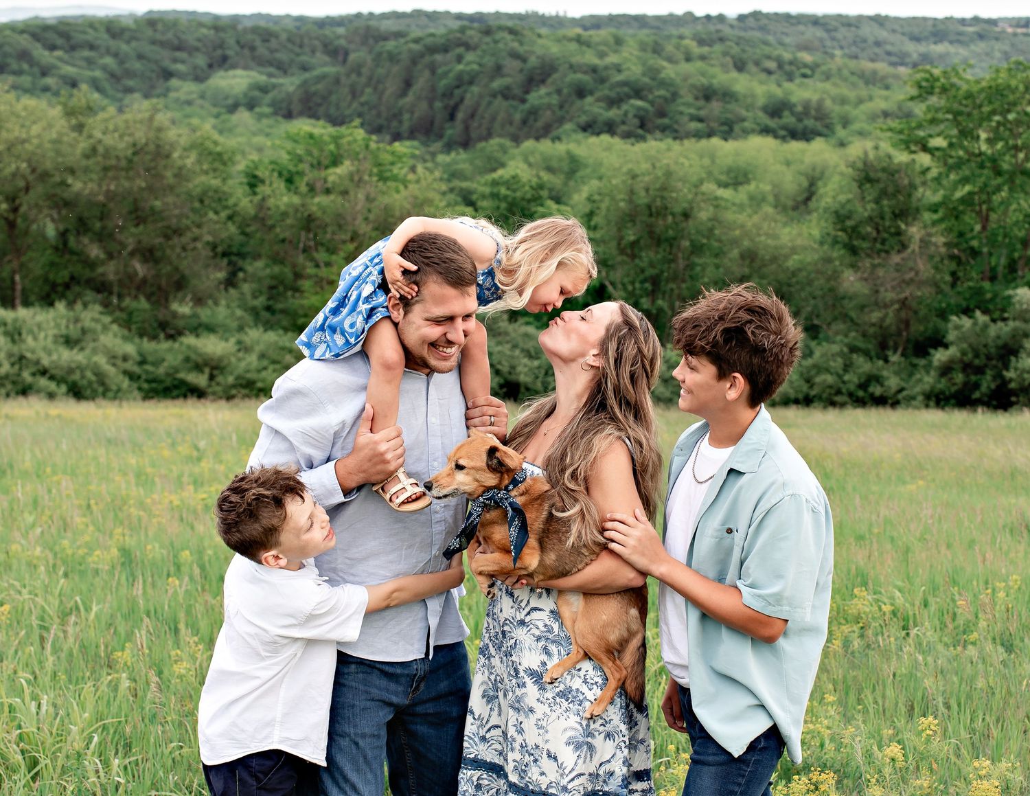Family members share joyful embraces and laughter while spending time together in a lush green summer meadow.