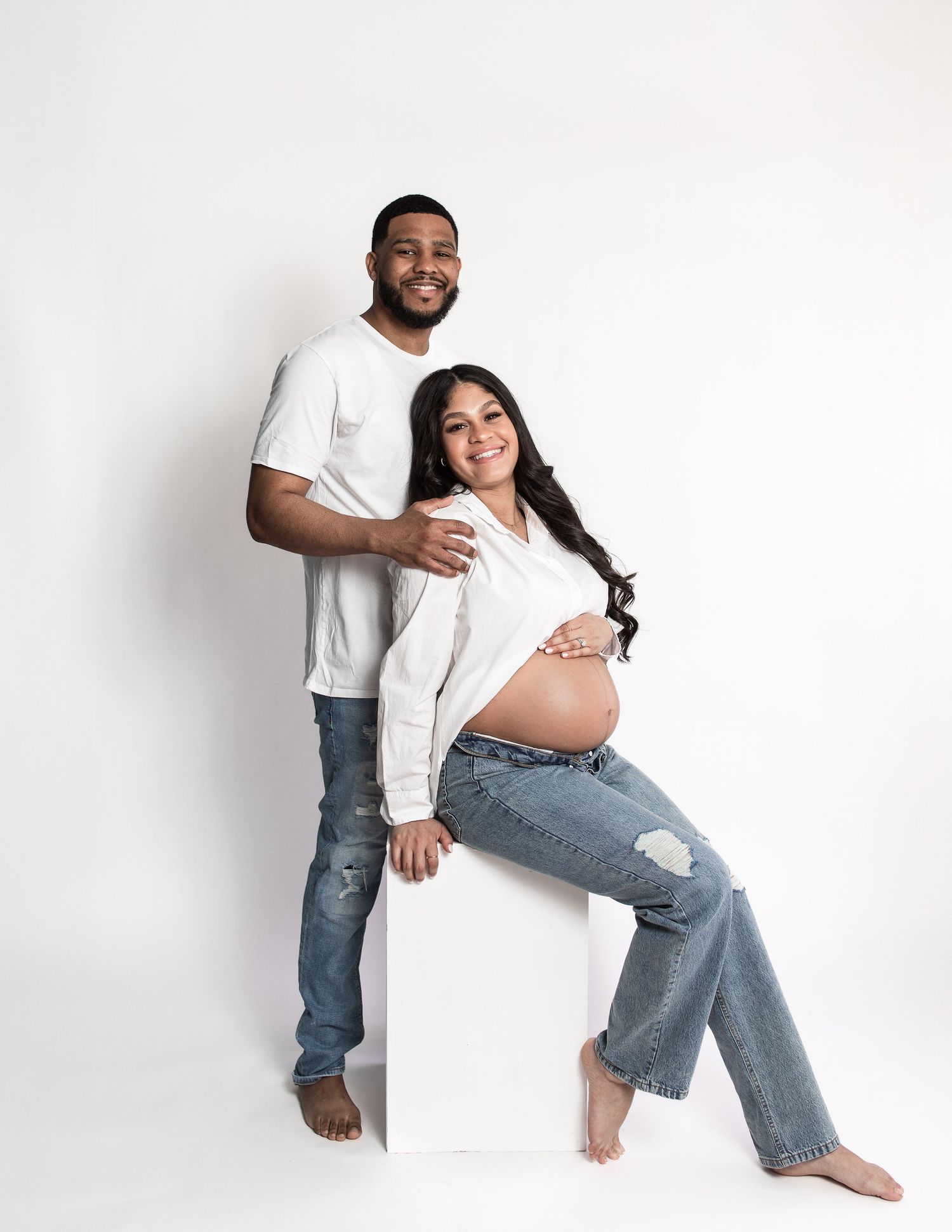 Candid maternity session with couple in jeans and white tops.