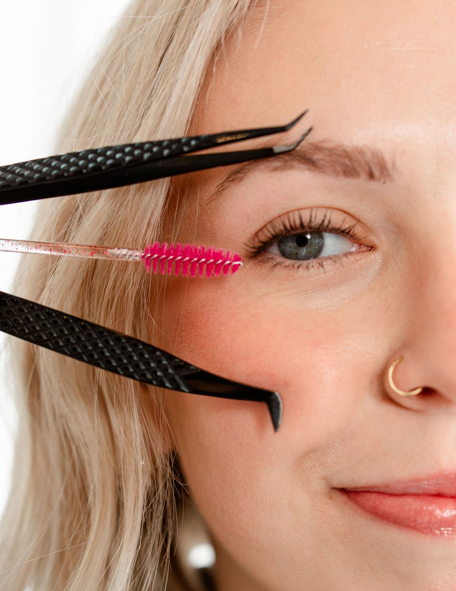 Close-up beauty shot showing the application of mascara to eyelashes using a pink wand against a white background.