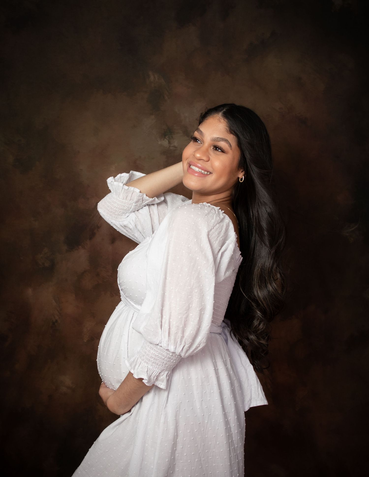 Elegant maternity portraits showing woman in white dress against dark background.