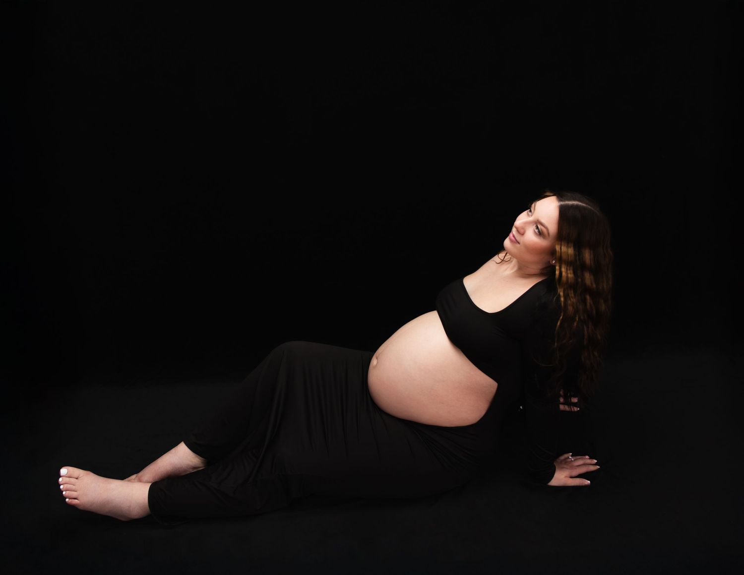 Maternity photo series in black and white against dark background showing pregnant woman in black dress.