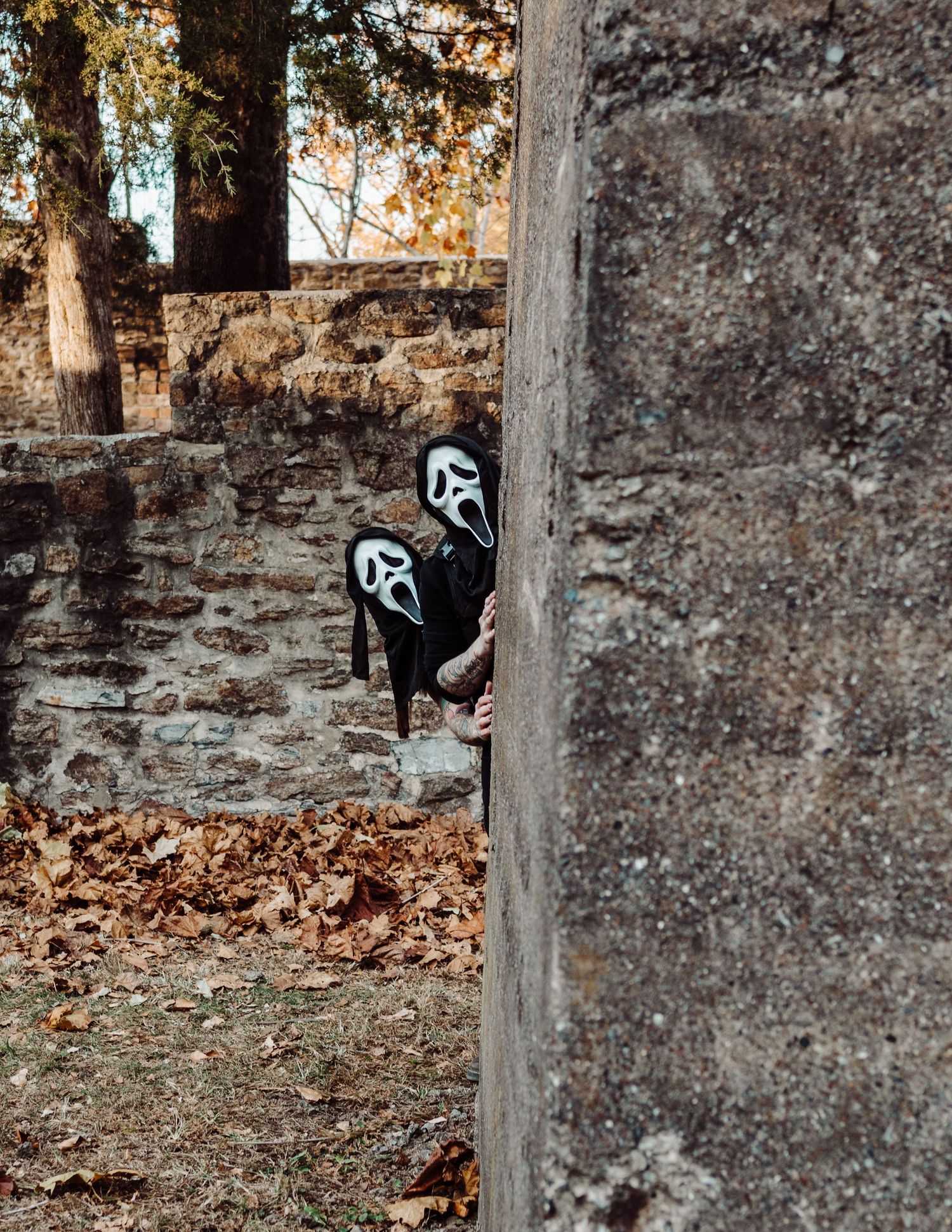 Spooky masked figures lurk among stone pillars in an atmospheric autumn setting.