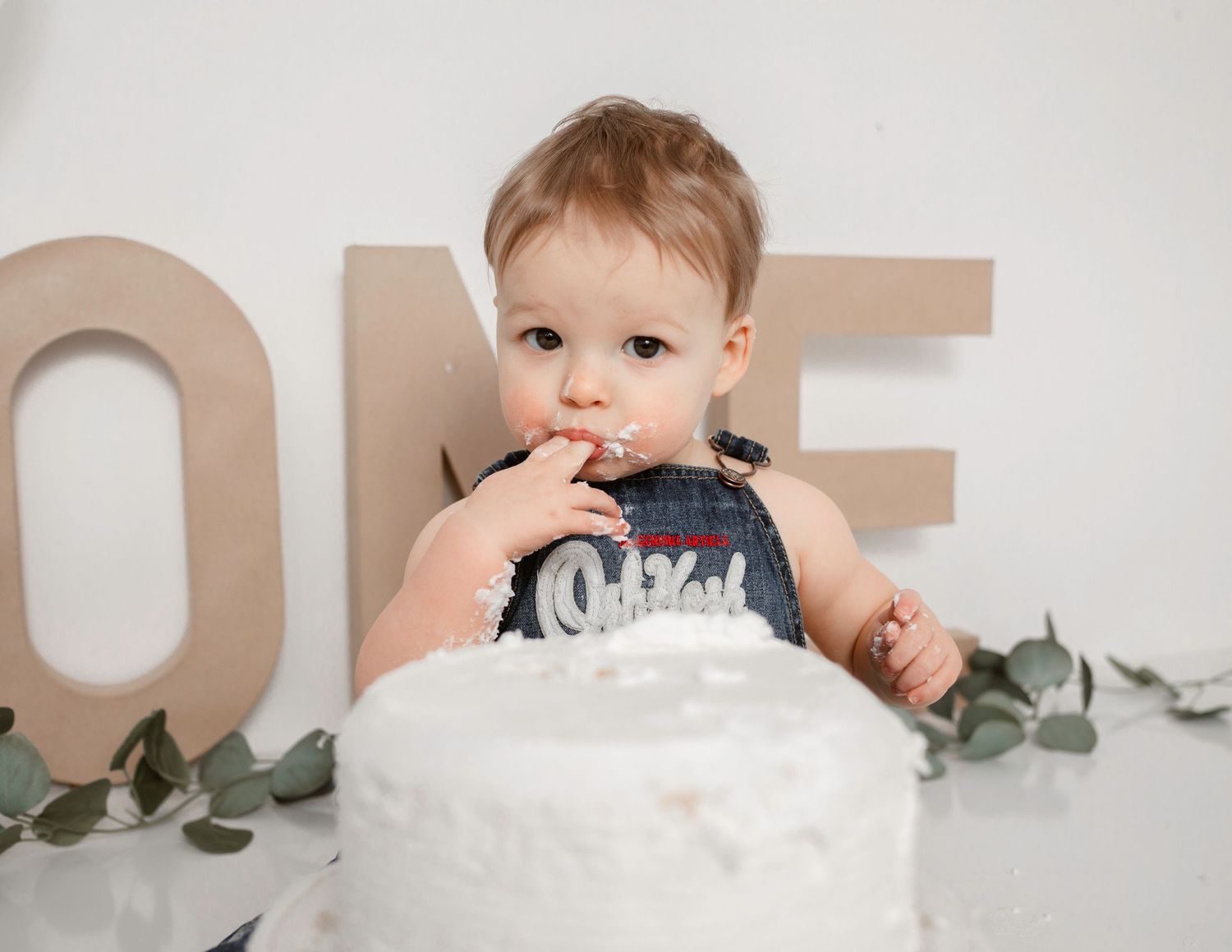 Baby tasting frosting from white cake during first birthday photo session.