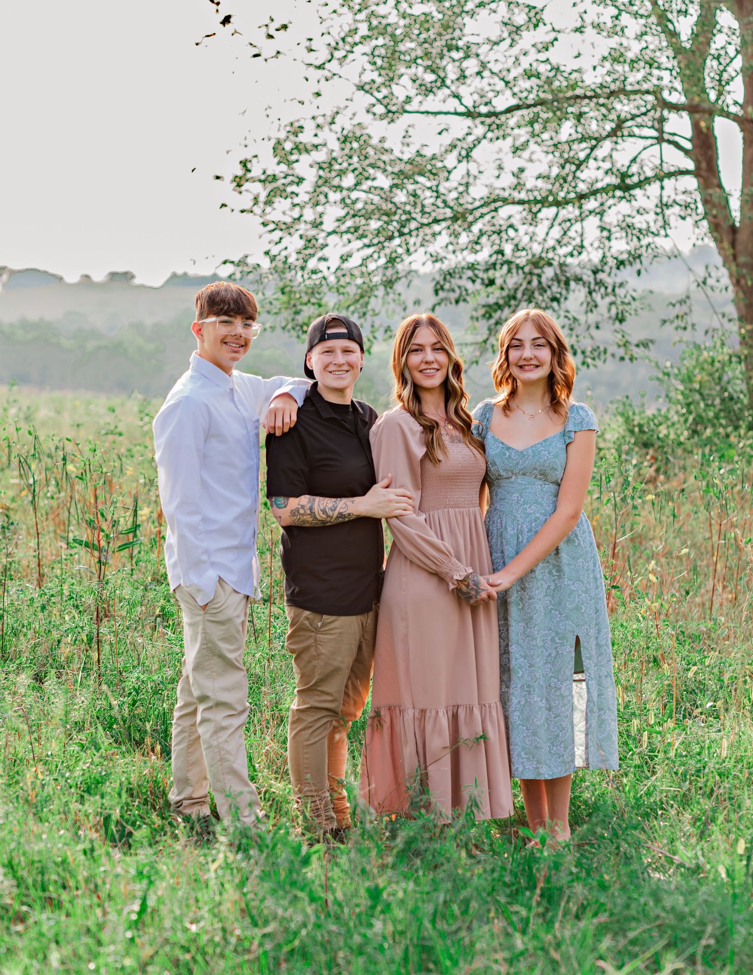 Family group portrait in coordinated outfits standing together in a lush green field.