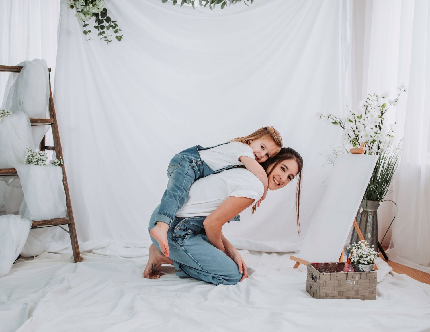 Minimalist white photography setup with wooden ladder and greenery accents.