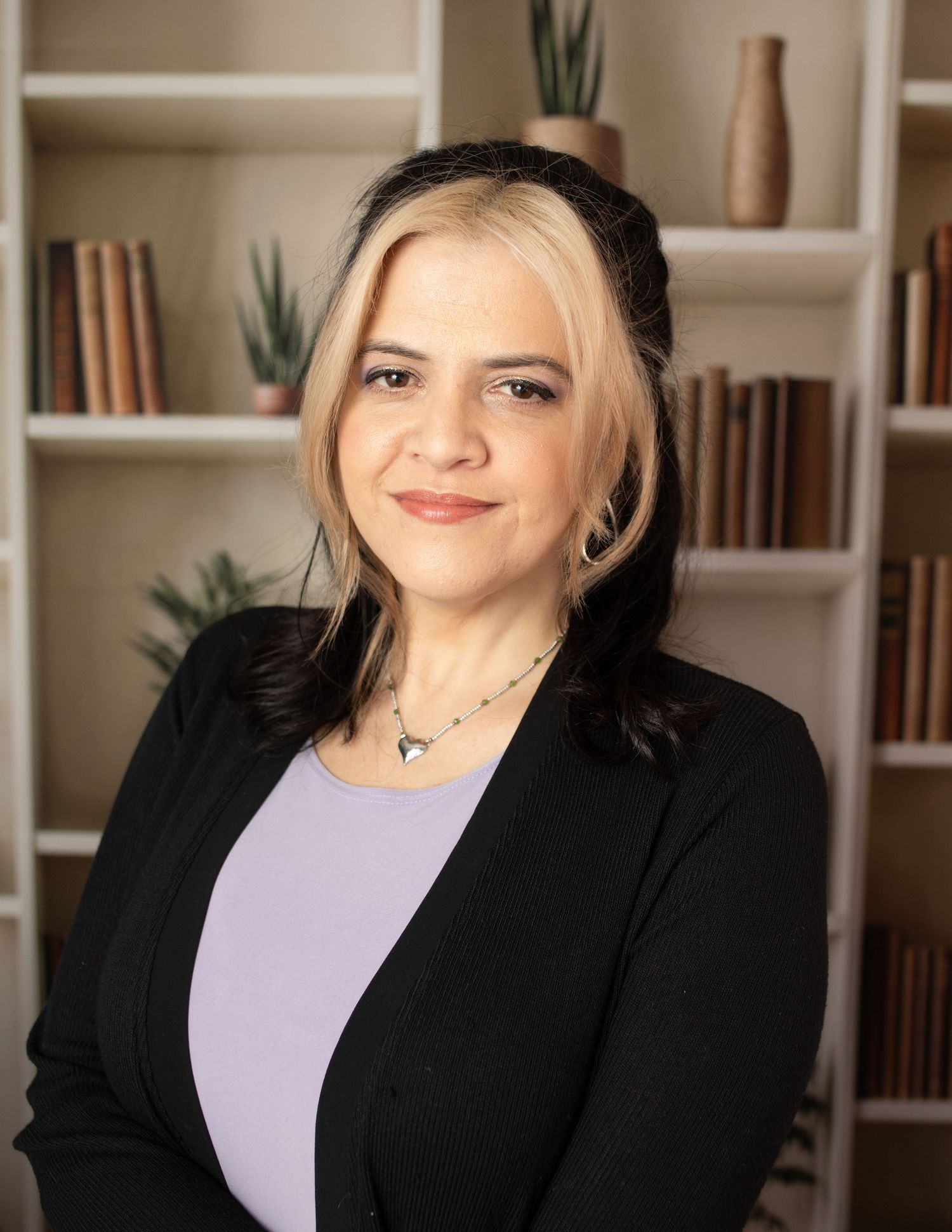 Professional woman in black blazer poses in front of modern bookshelf.