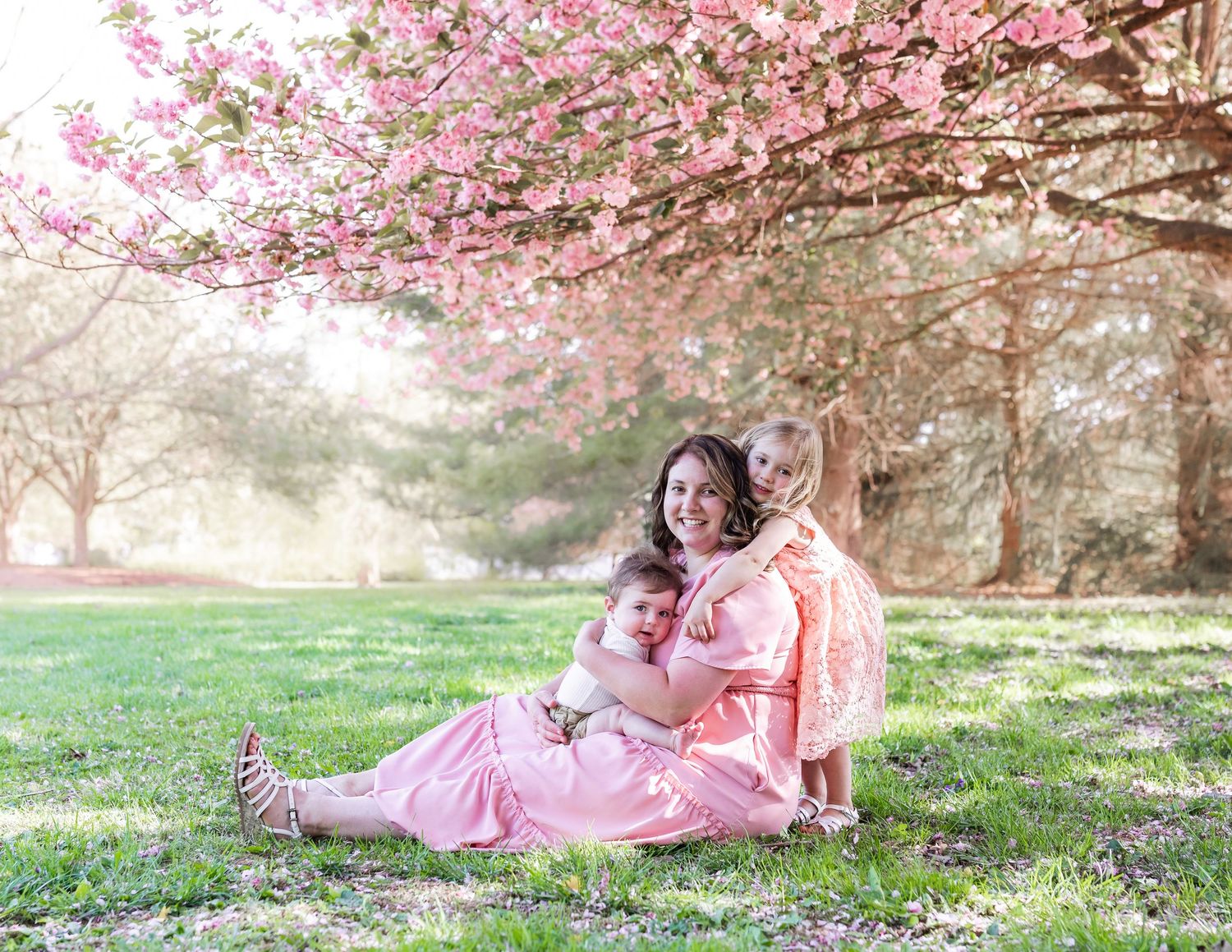 Candid moments captured on grass beneath flowering cherry trees in soft pink tones.