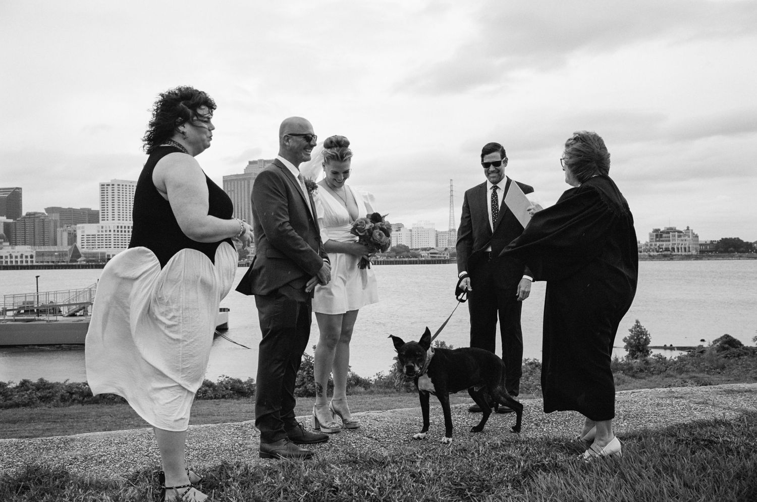 Small wedding ceremony with guests and a dog gathered by the waterfront.
