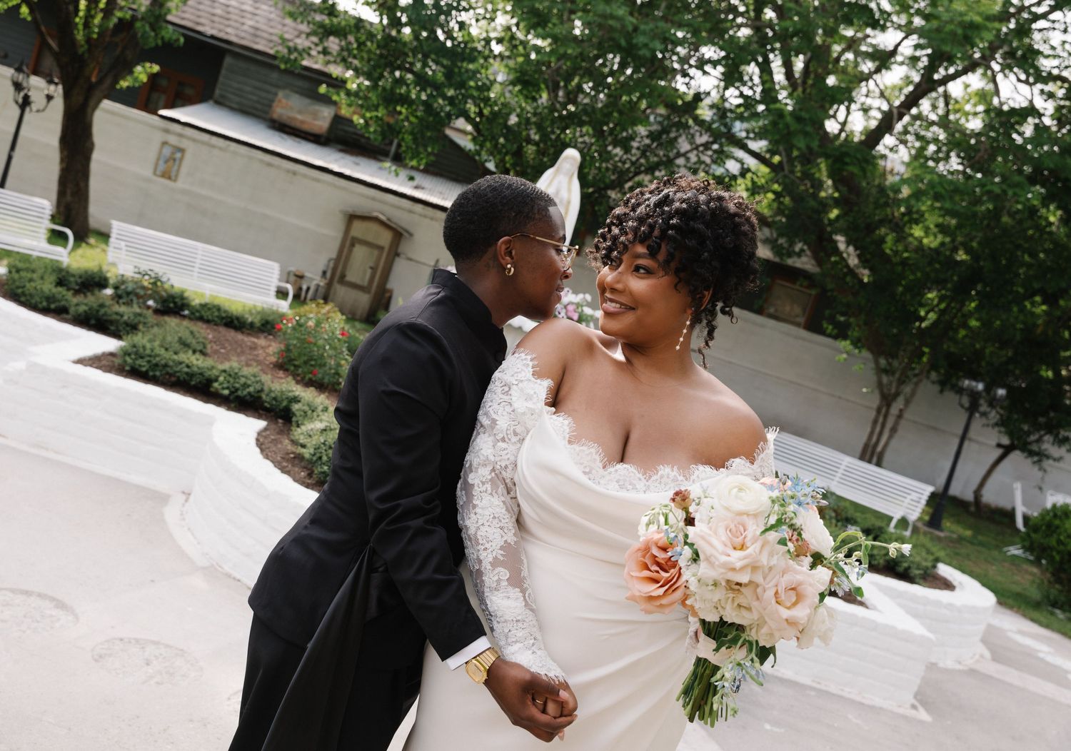 A joyful Black couple shares a romantic moment on their wedding day, bride in lace gown holding blush bouquet.