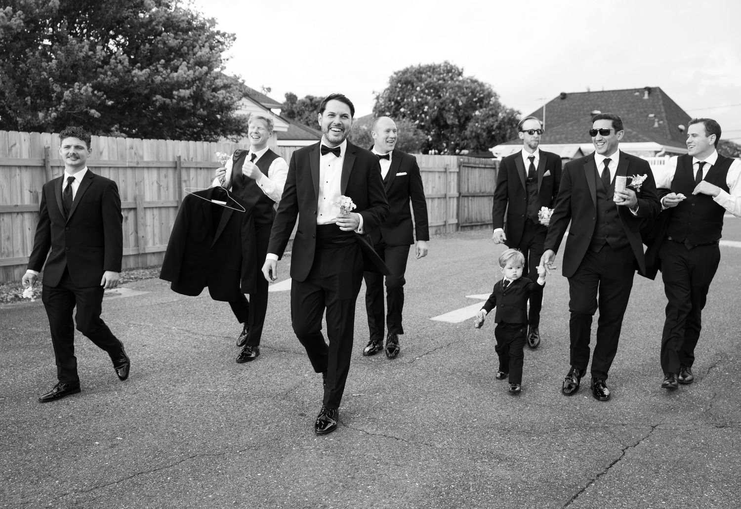 Groomsmen walking in formation across a grassy field in black suits.