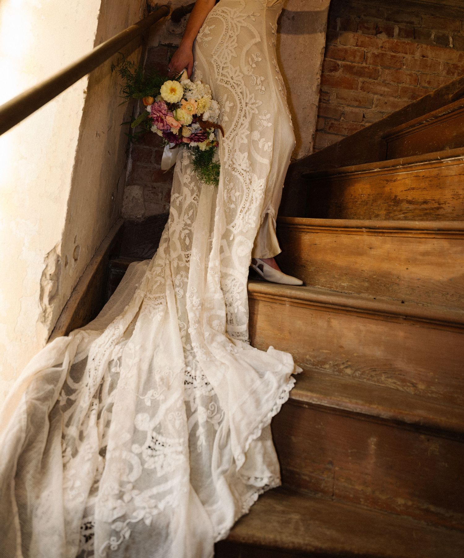 Close-up detail of a white lace wedding dress train cascading down wooden stairs.