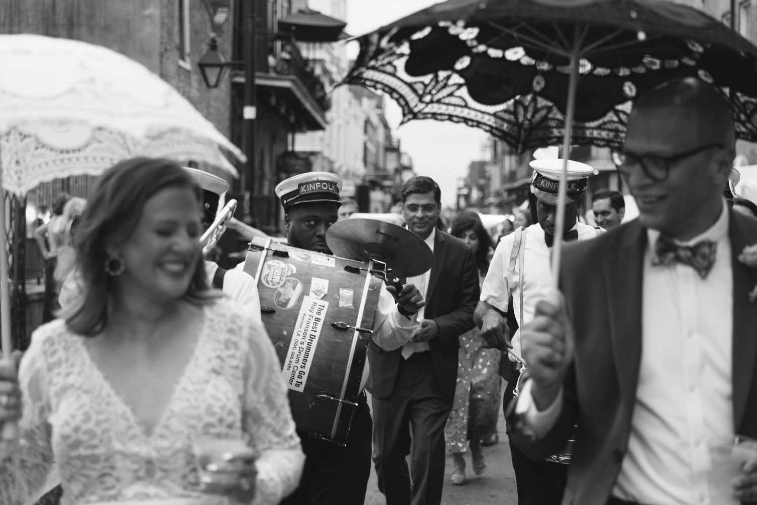 Black and white photo of a New Orleans second line wedding parade with bride, groom, and jazz musicians on a busy street.