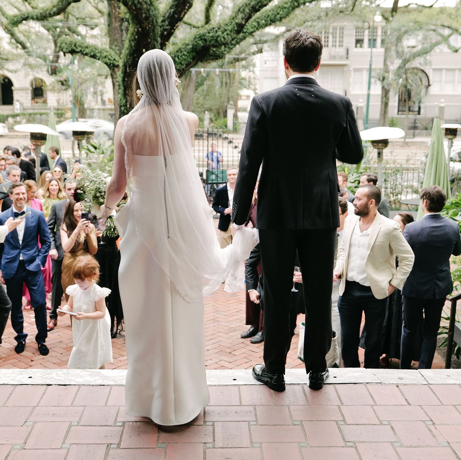 Wedding guests walk along a stone pathway through a garden setting during an outdoor ceremony.