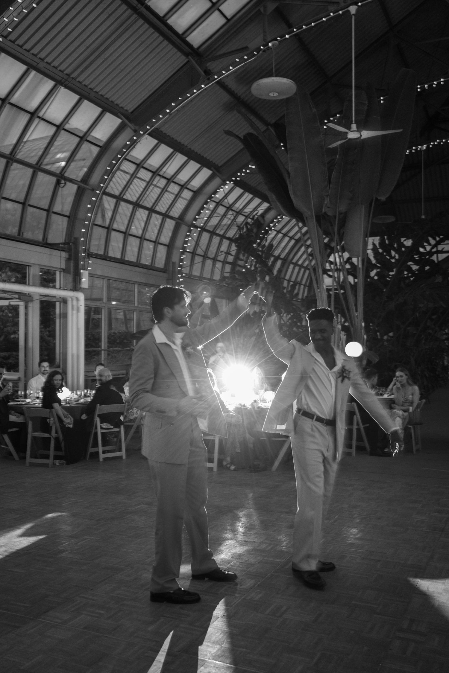 Married couple dancing their first dance in an elegant arched venue with string lights overhead.