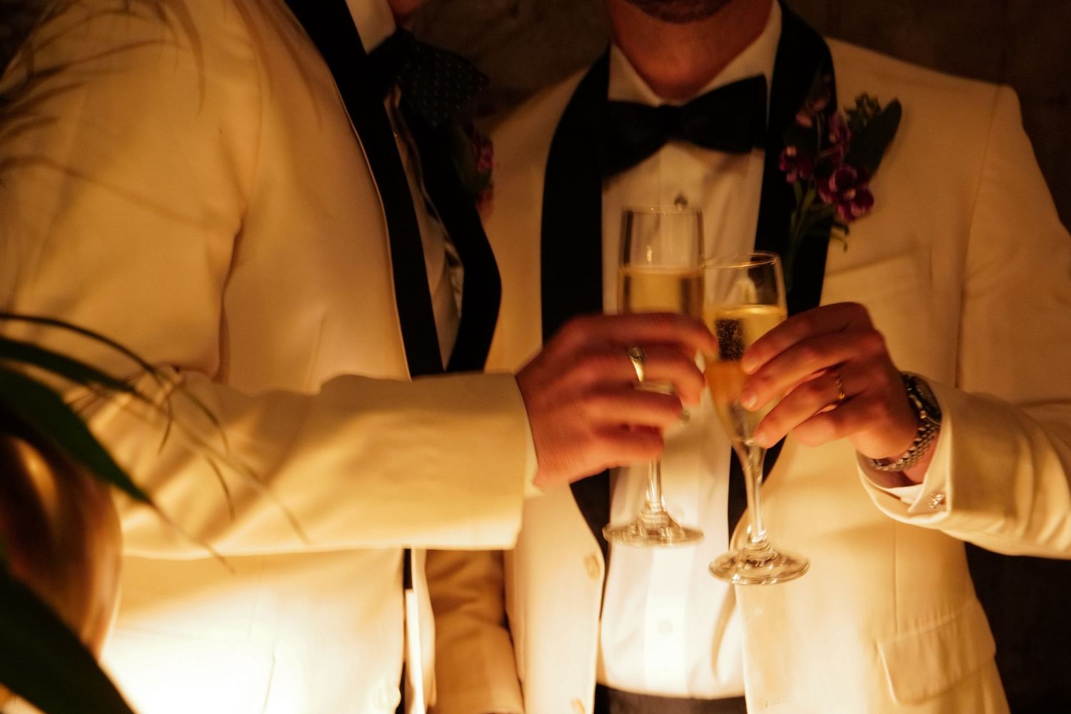 Wedding grooms raise champagne glasses for a celebratory toast at an elegant wedding reception.