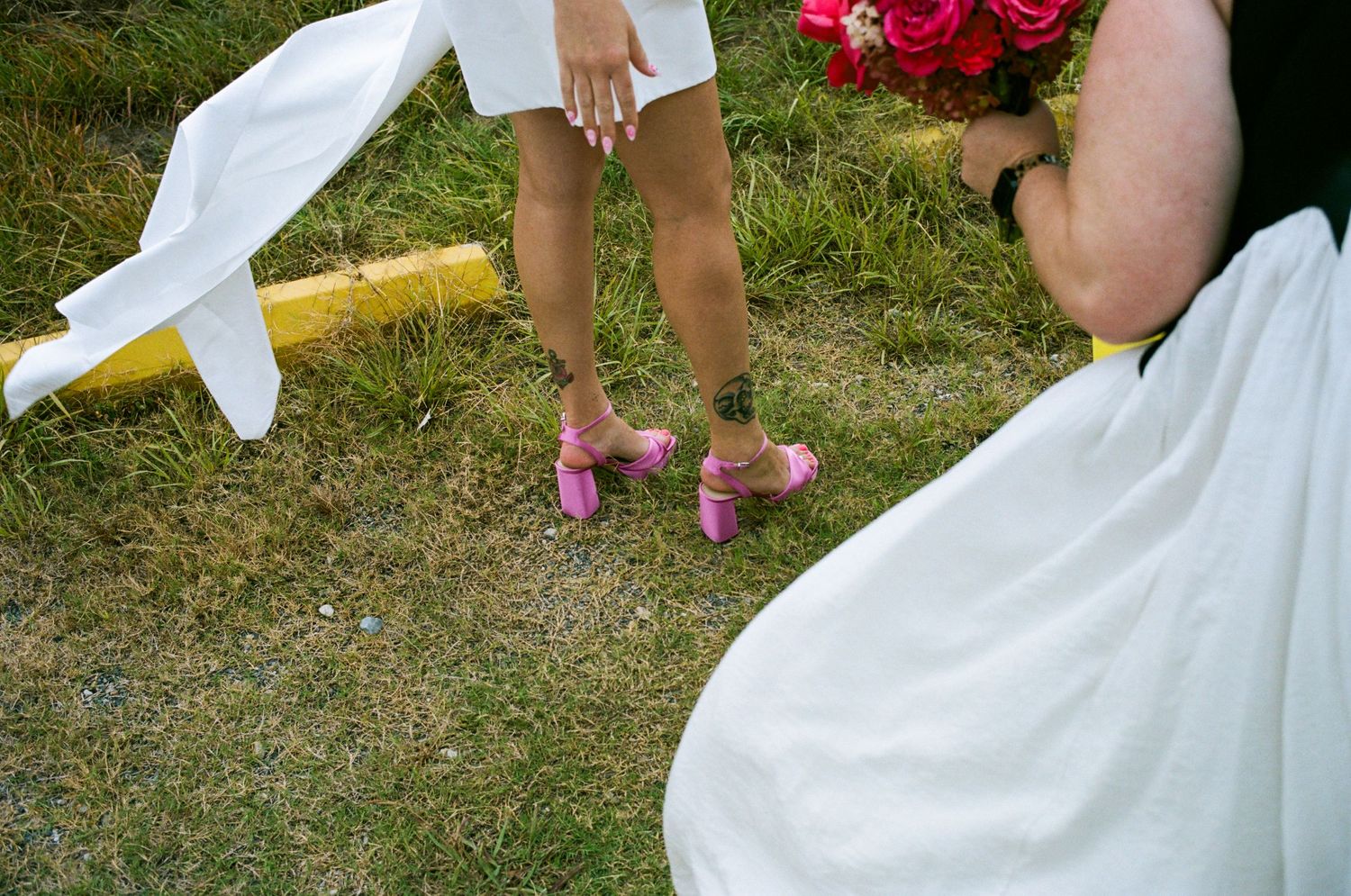 Detail shot of pink heels and white dress hem on grass with roses.