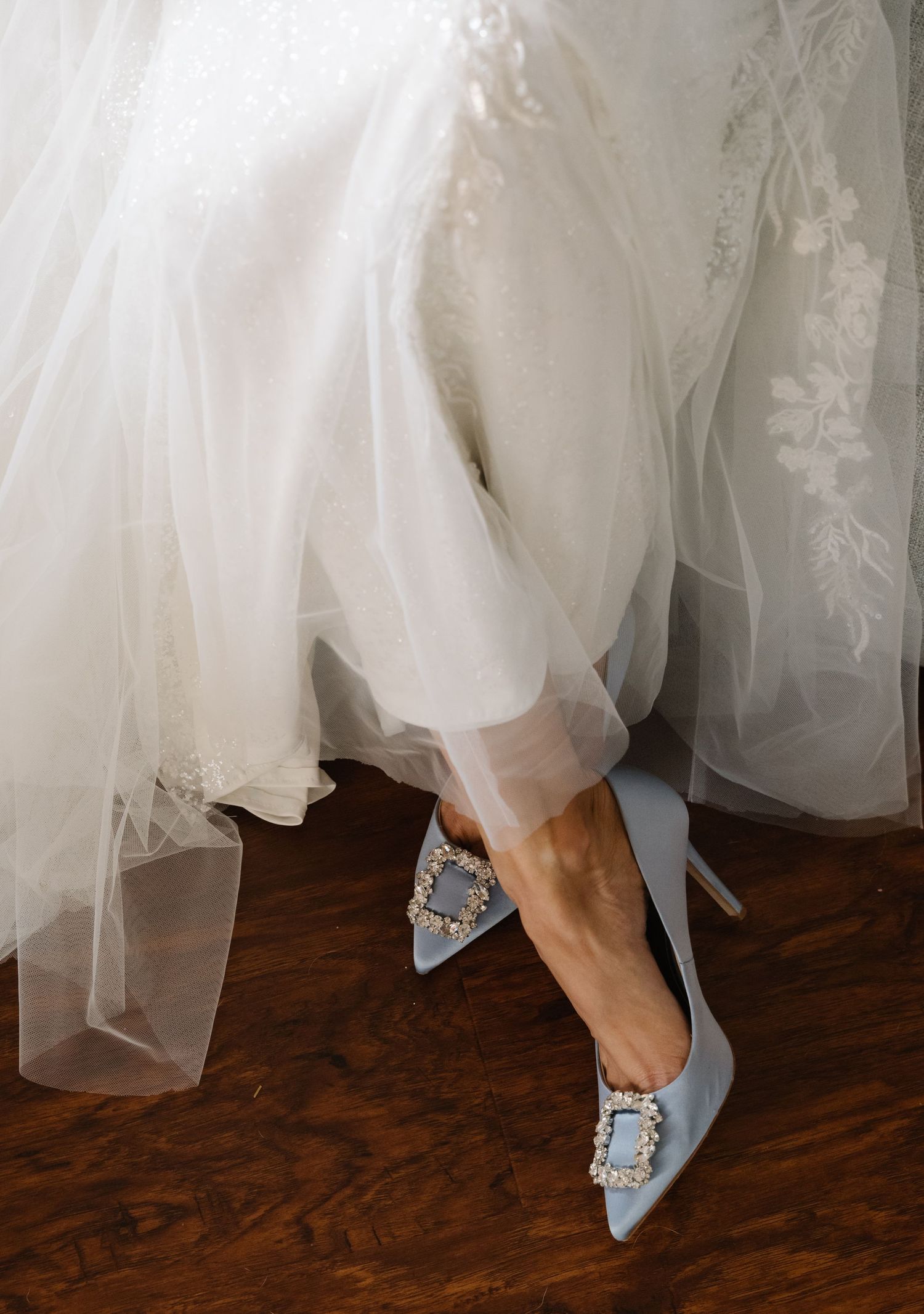Close-up shots of ornate blue wedding shoes with crystal details under a white dress.