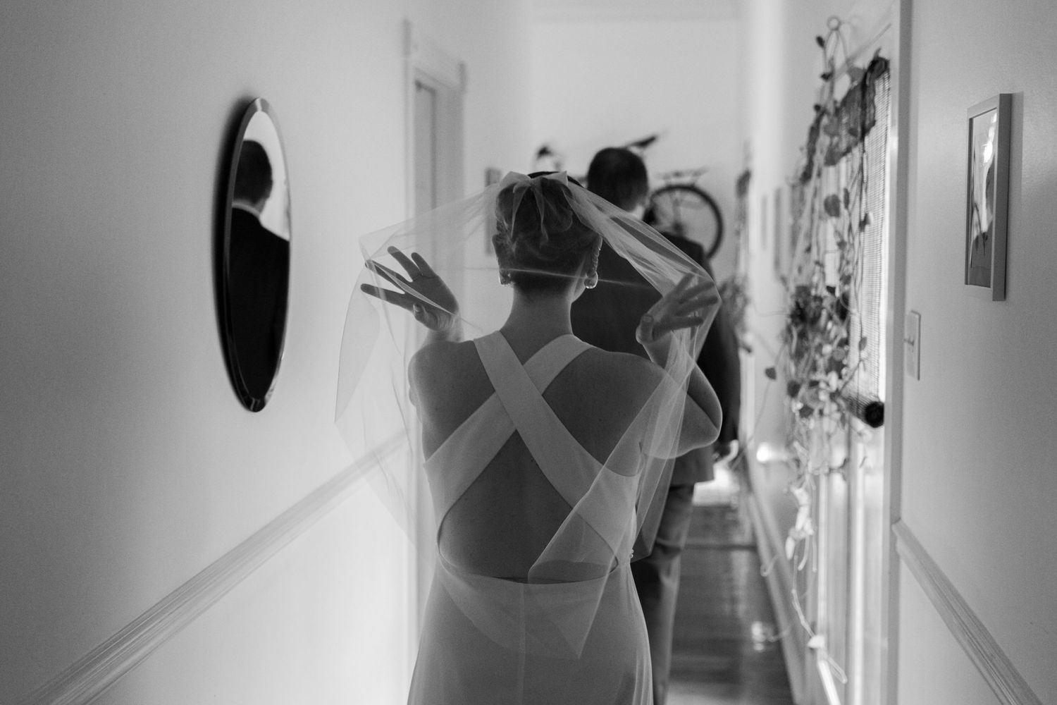 Black and white hallway scene of a bride with natural light streaming through windows.