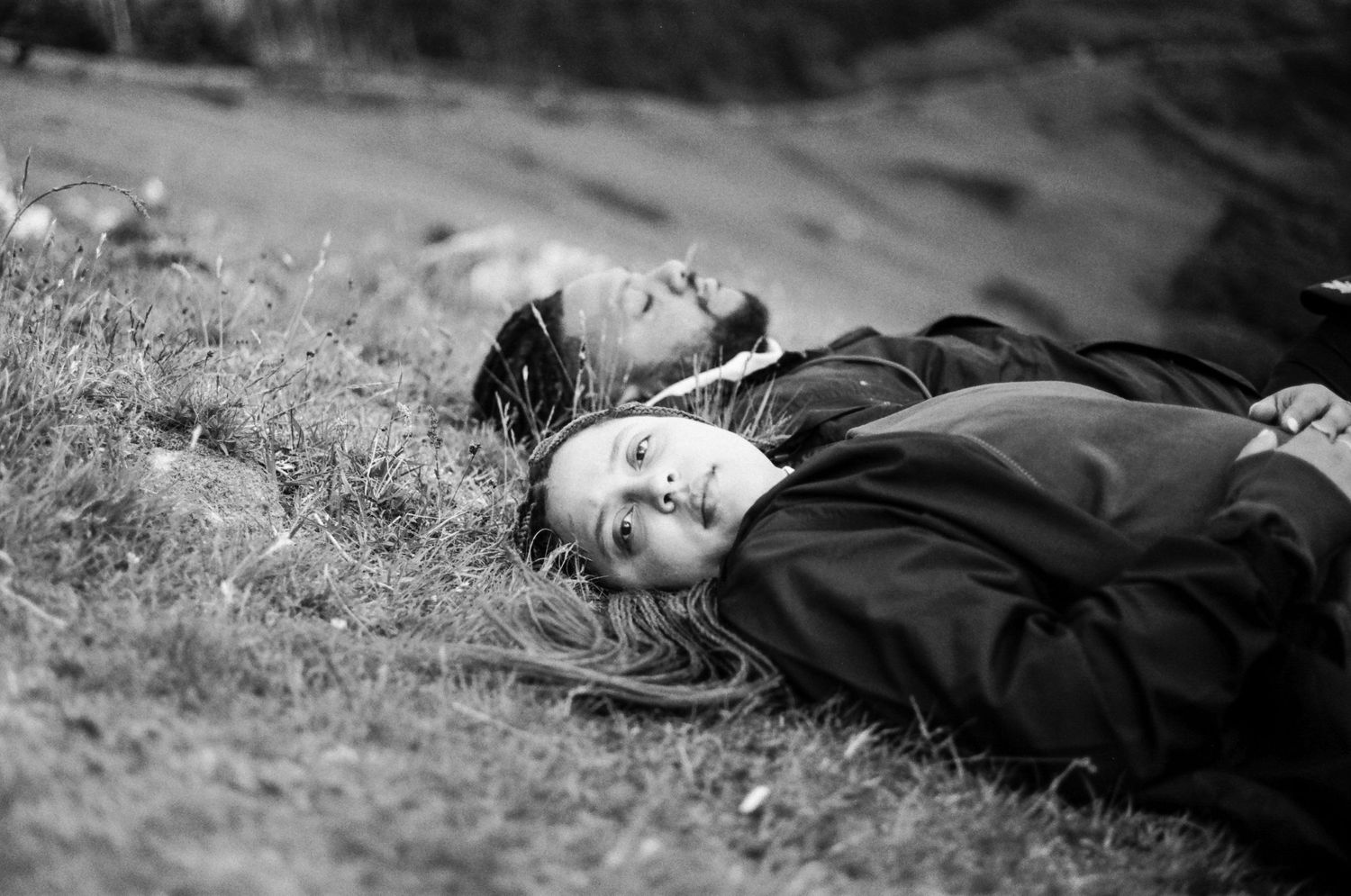 Two people lying on grass in a black and white photo, relaxing outdoors on a hillside.