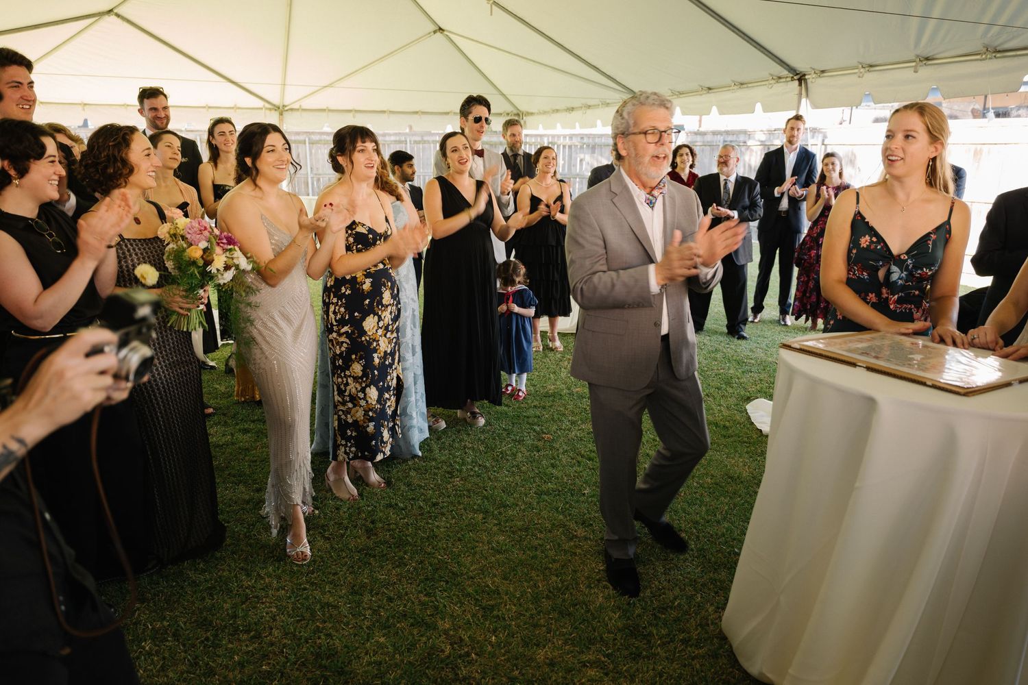 Wedding guests in formal attire gathered under a white tent for a celebration.