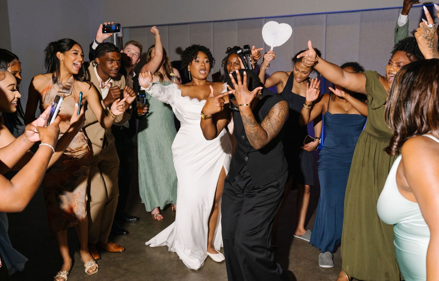 Bride and groom dancing joyfully at wedding reception surrounded by cheering guests in elegant attire.