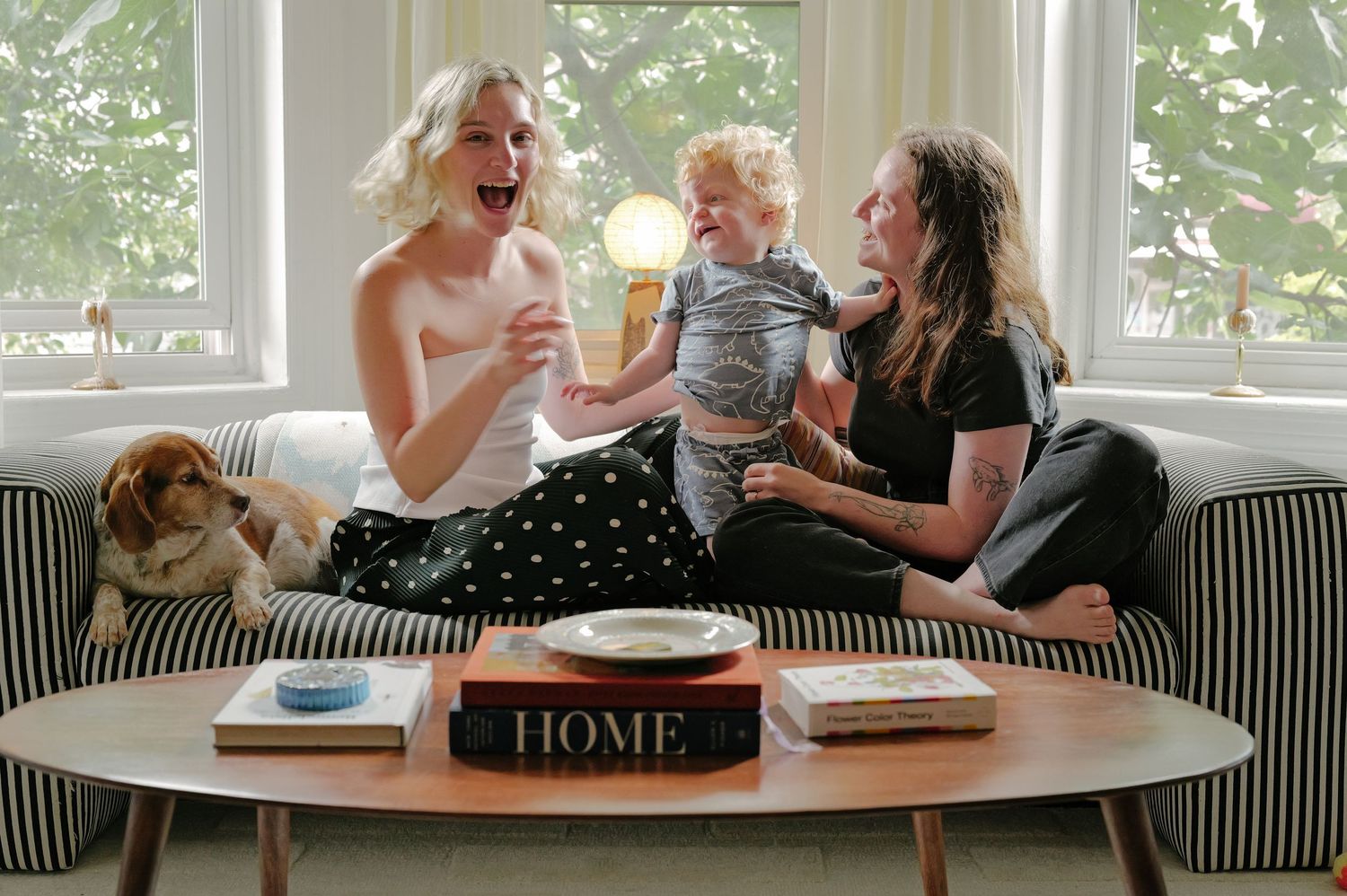 Couple sitting on a couch with a small child and dog in a bright, sunny living room.