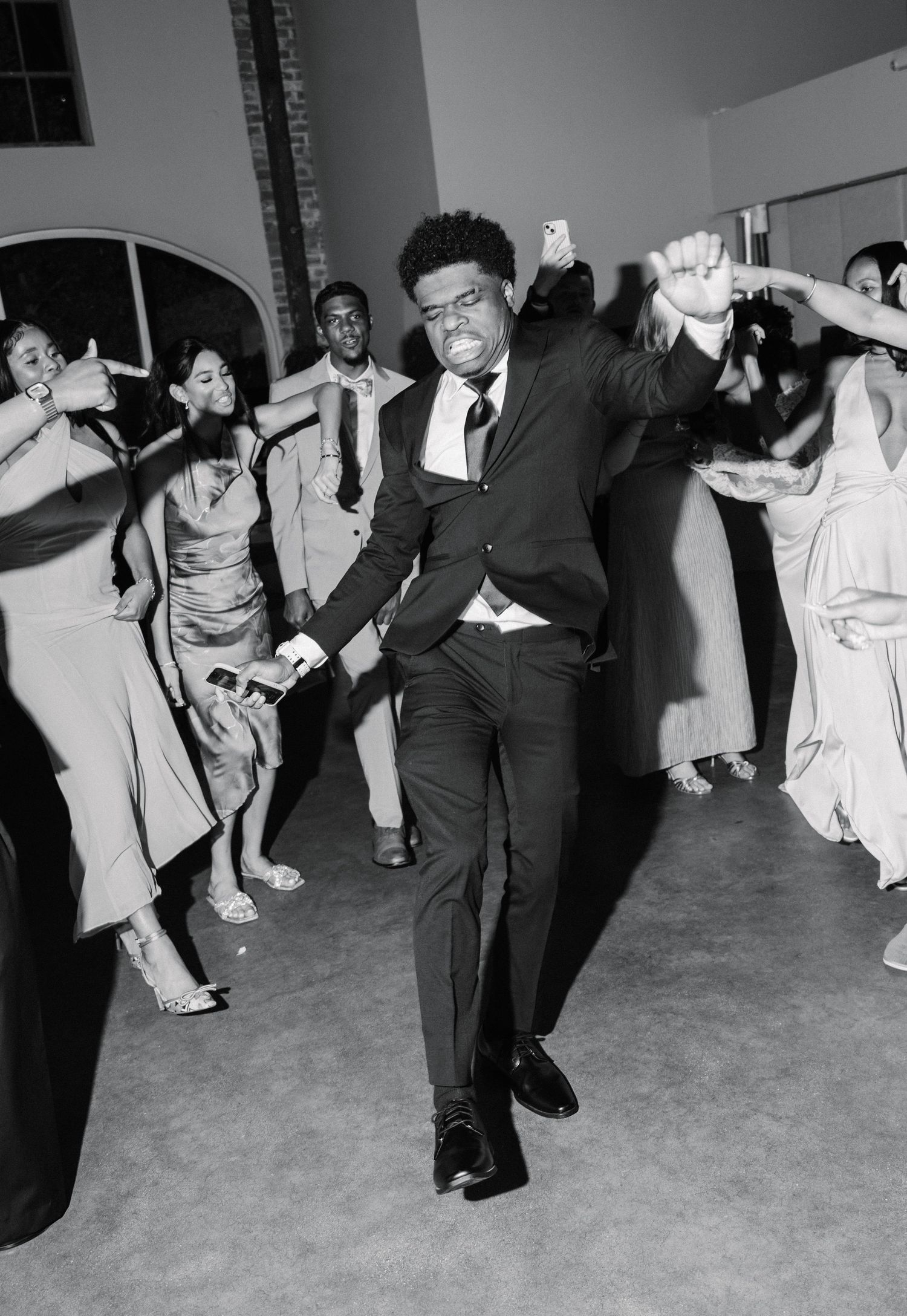 Man in suit dancing energetically at a formal event, surrounded by elegantly dressed guests on the dance floor.