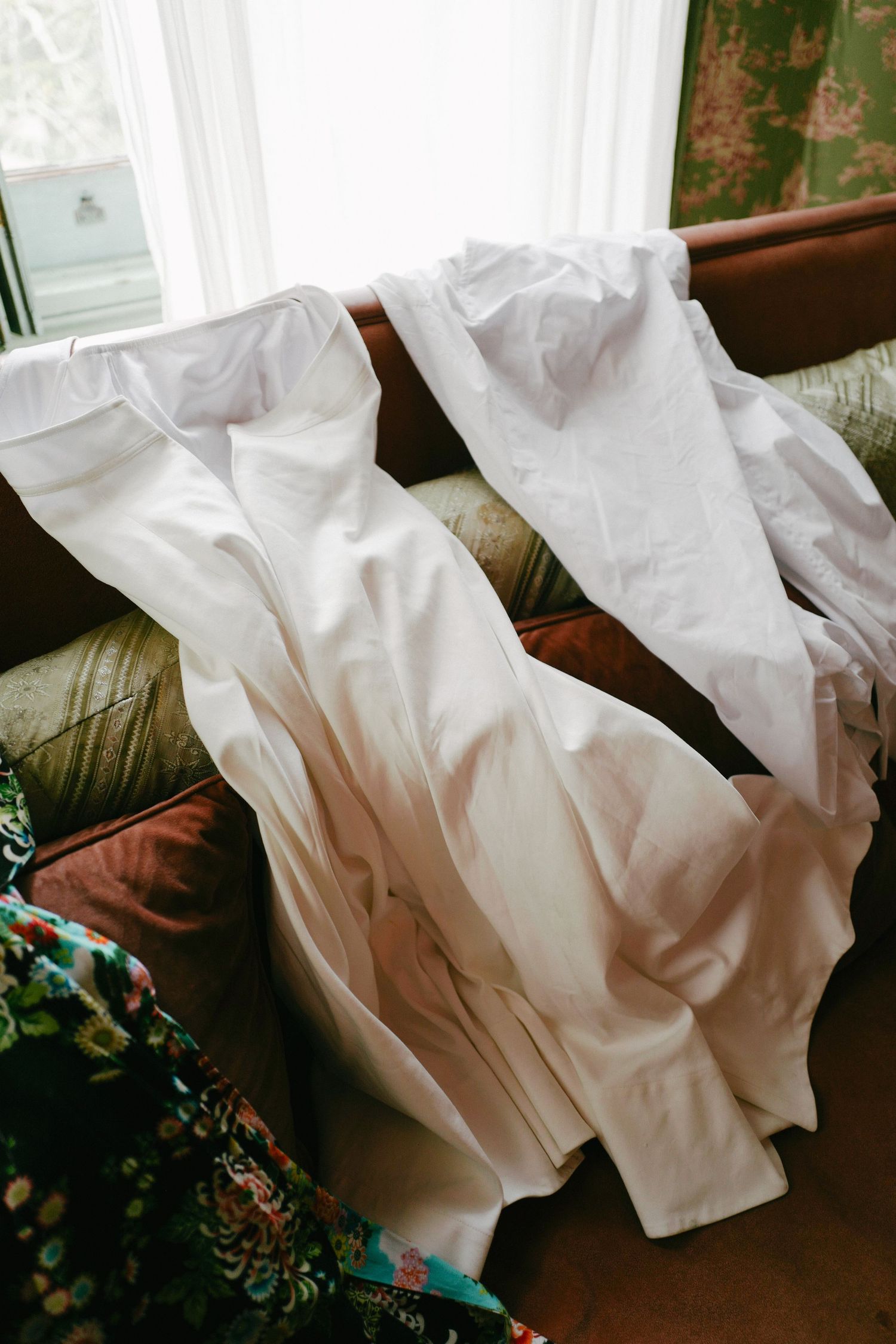 Wedding dress laid out on a floral patterned couch in natural daylight.