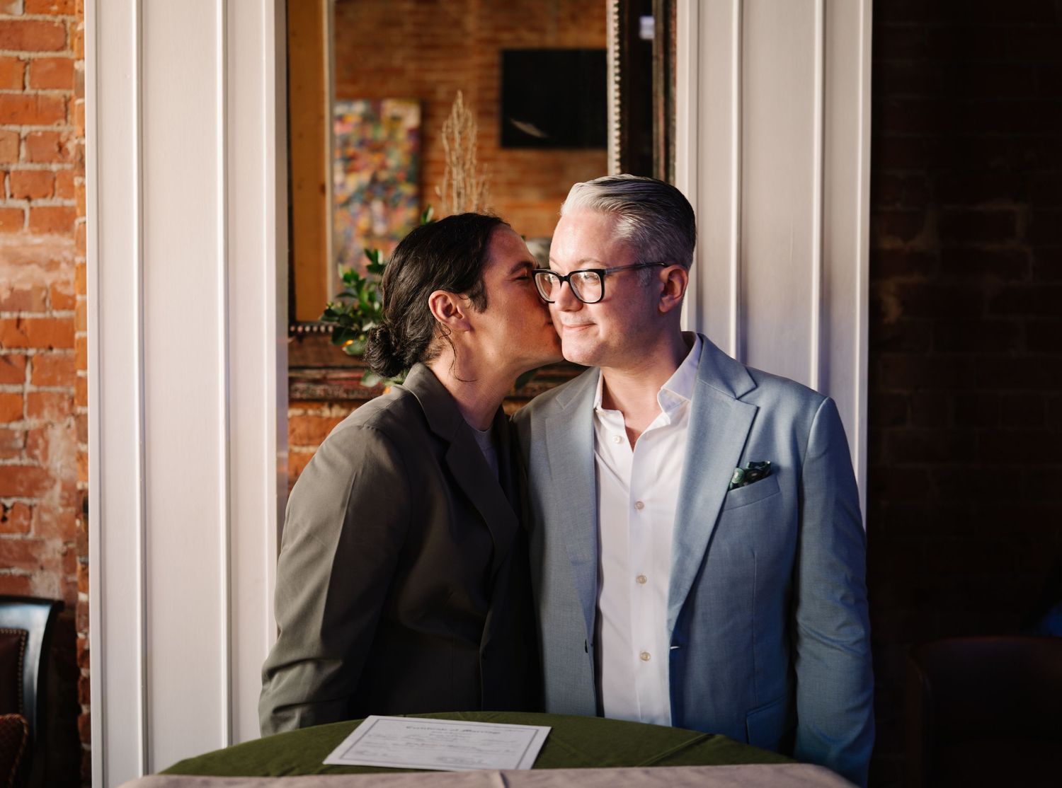 A tender moment shared between a married couple in a brick-walled room.