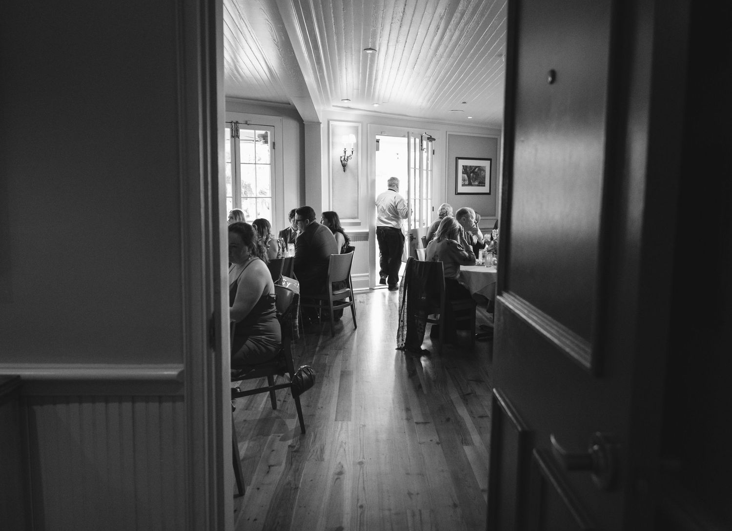 Black and white photo of diners enjoying meals in a cozy restaurant dining room with hardwood floors.