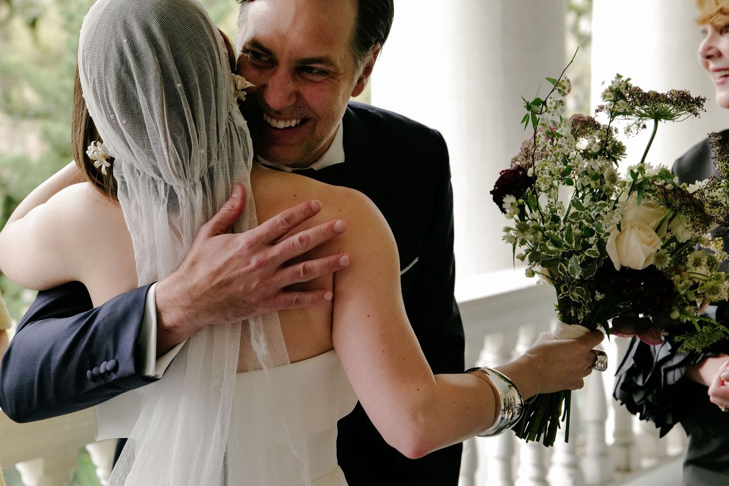 Wedding party bouquets with white and green florals with a bride hugging her dad.