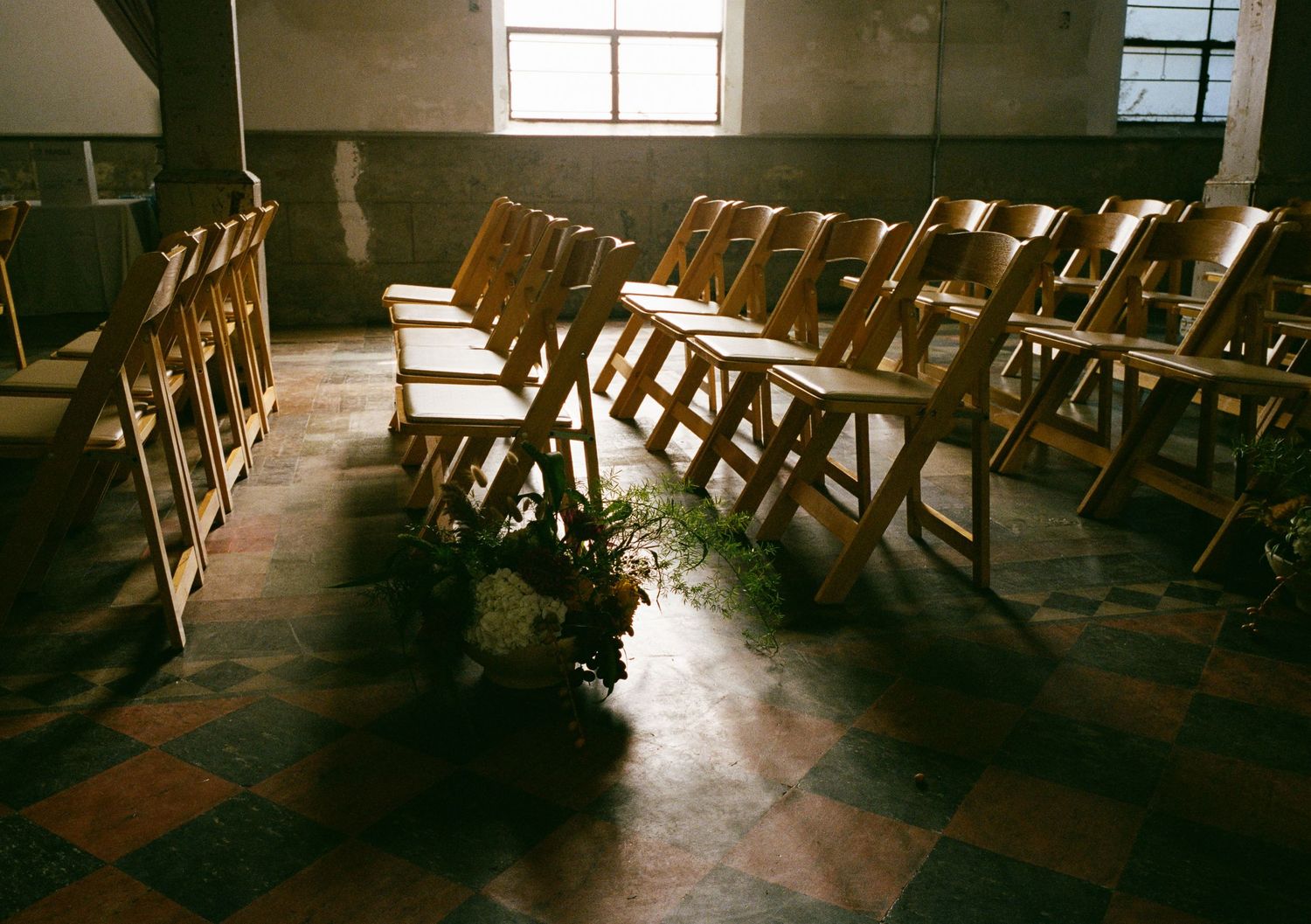 Rows of wooden folding chairs in an empty wedding venue with sunlight streaming through windows.
