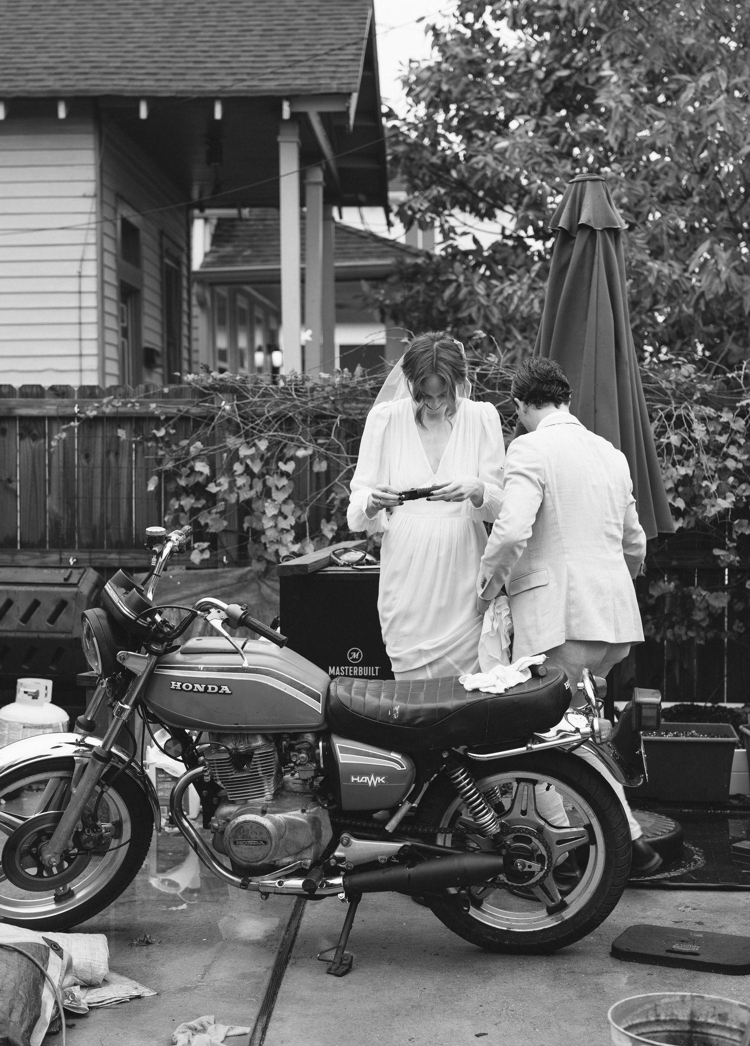 Black and white photo of two people working on a Honda motorcycle in a residential backyard.