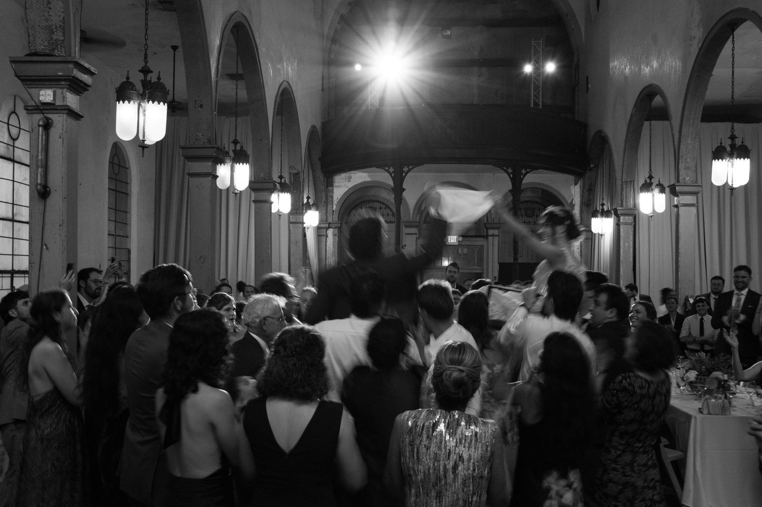Large crowd gathered in an ornate hall with vaulted ceilings and chandeliers dancing at a wedding reception in New Orleans.