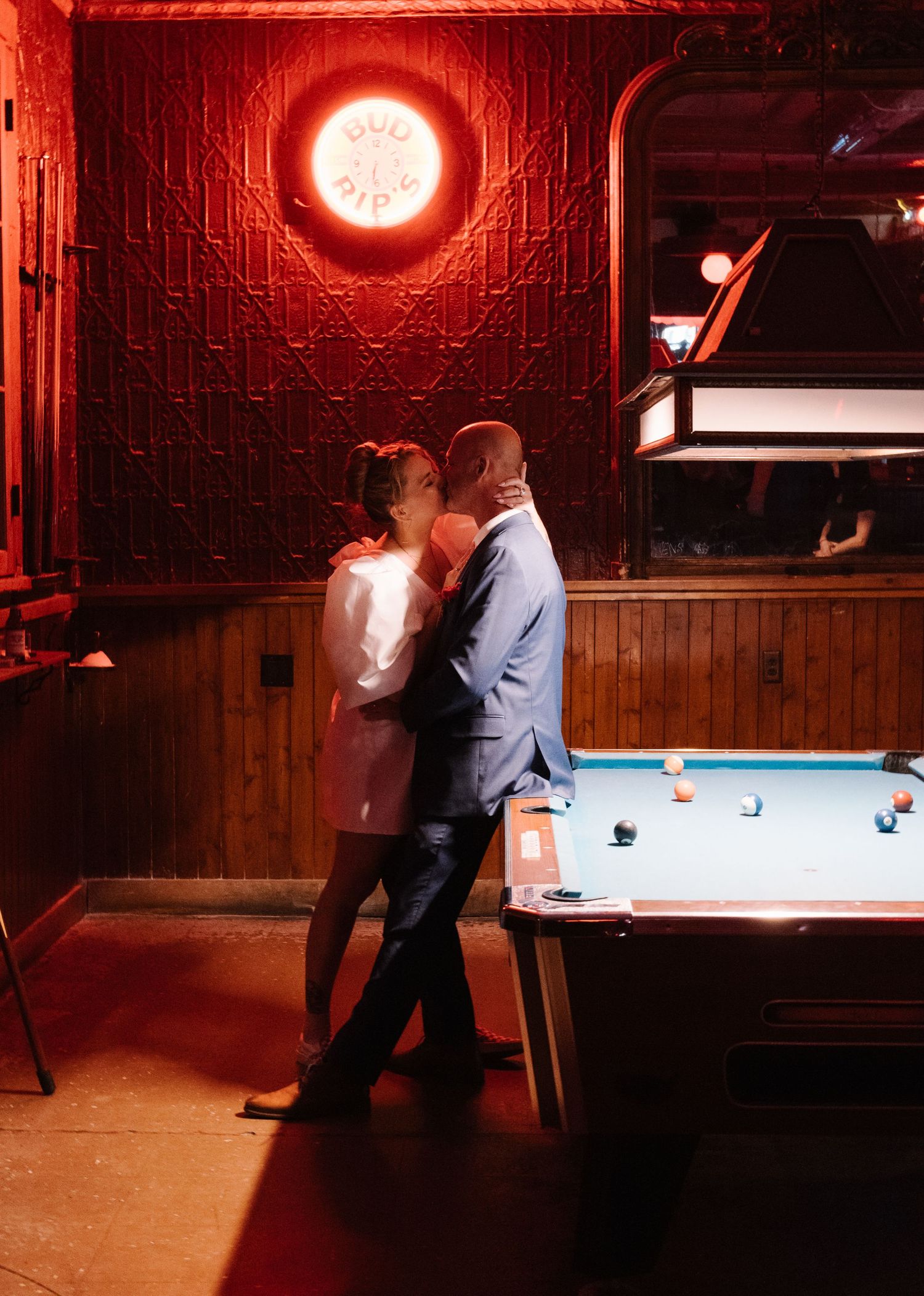 Couples dancing in a dimly lit bar with red neon lighting and pool tables.