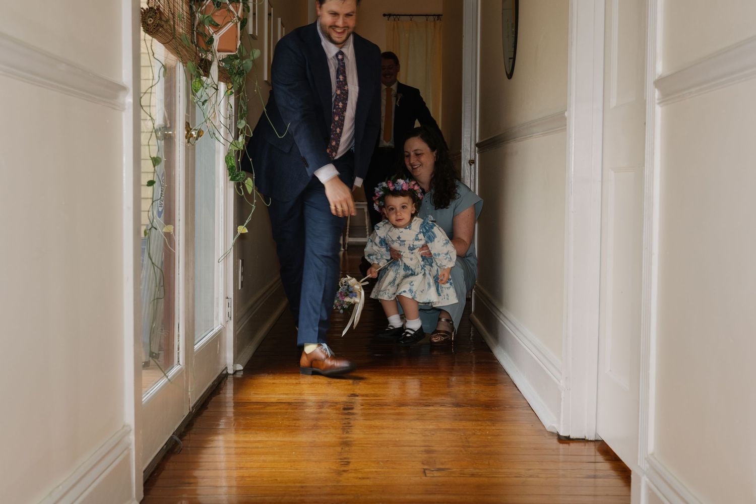 Long indoor hallway with hardwood floors and white walls showing movement of flower girl.