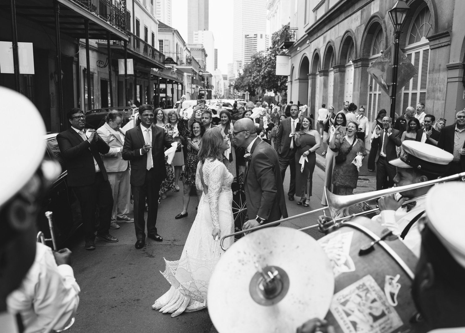 Black and white photo of a wedding procession on a New Orleans street with a jazz band and guests celebrating outdoors.