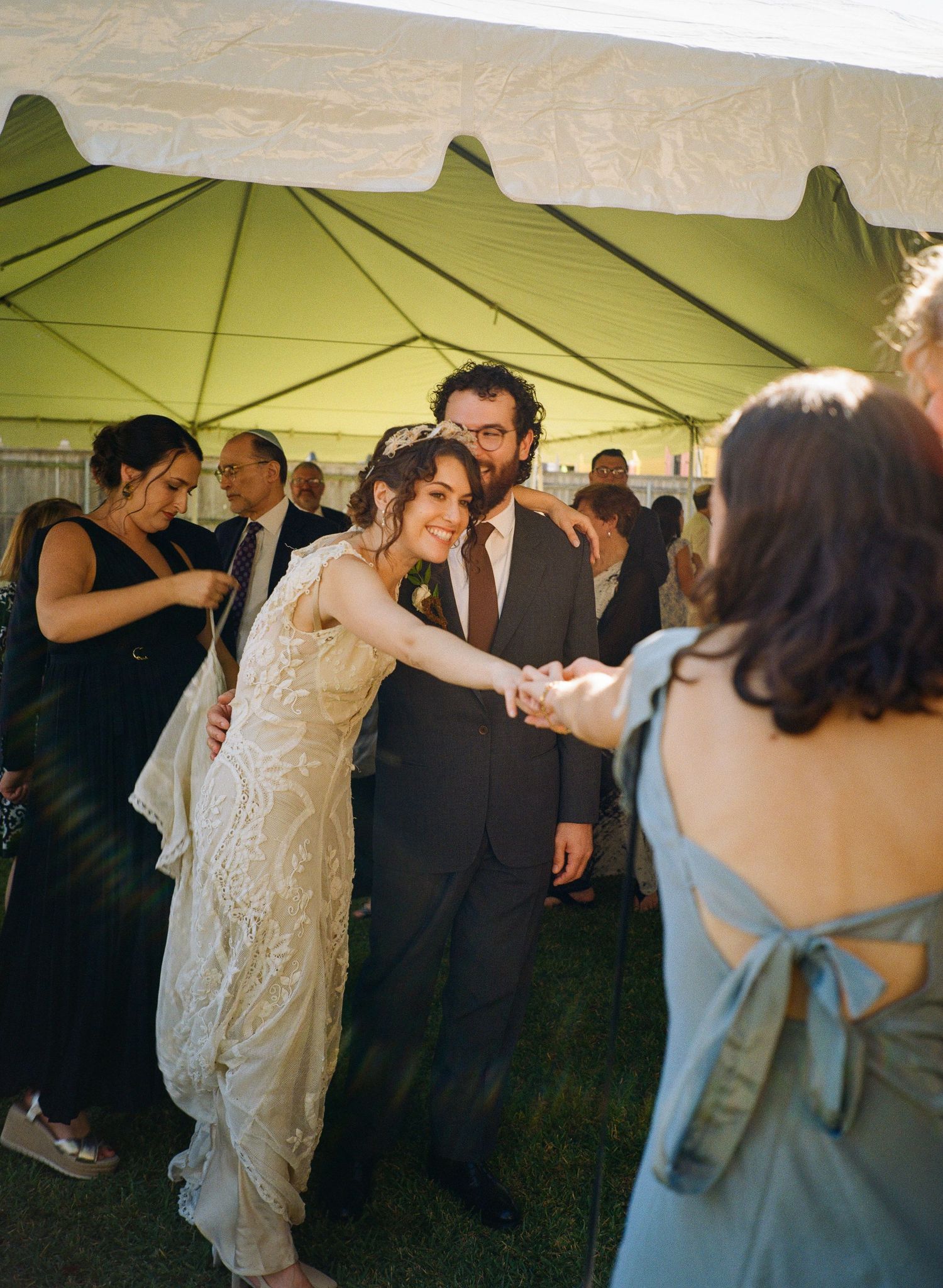 Wedding guests dancing under a white outdoor tent during a celebration.