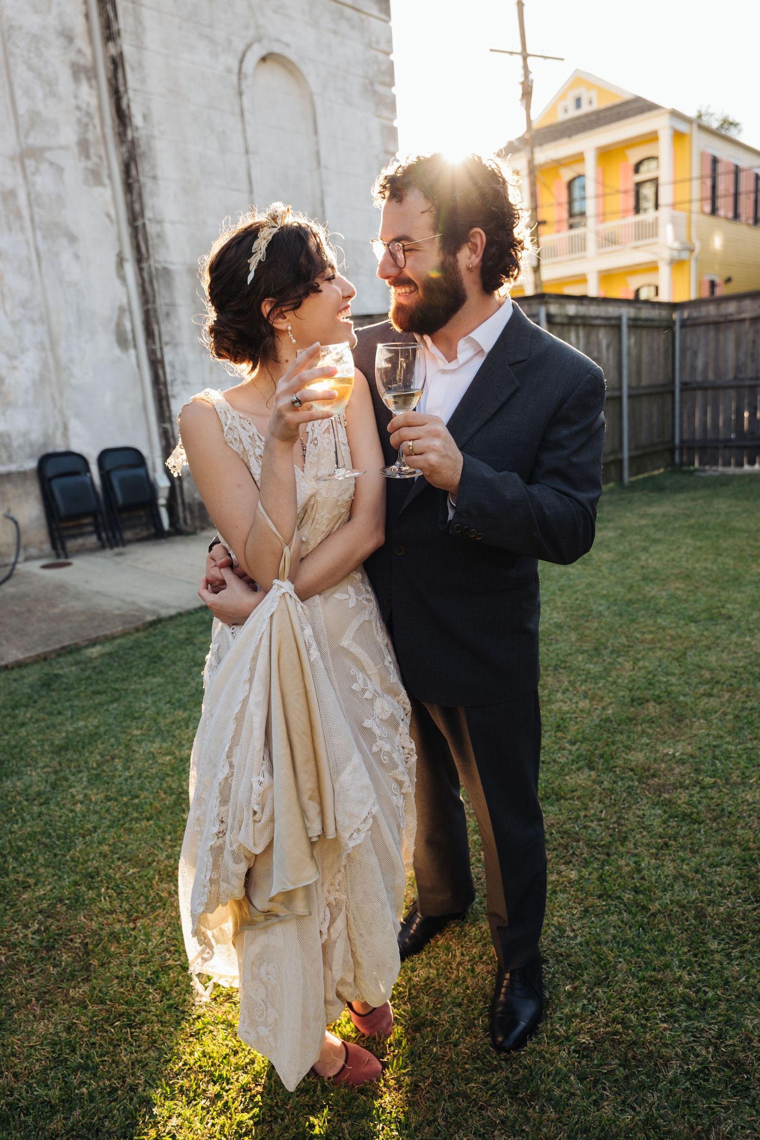 A newly married couple shares champagne outdoors at sunset with a yellow building in the background at The Marigny Opera House in New Orlean