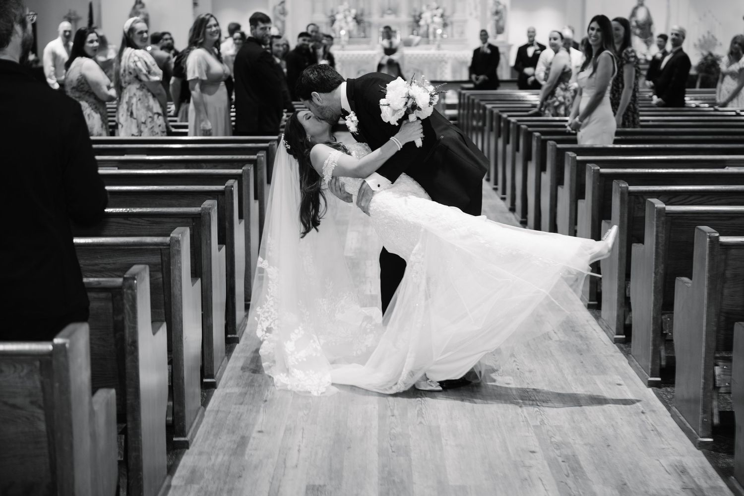 Wedding ceremony taking place in a traditional church with white decorations and wooden pews.