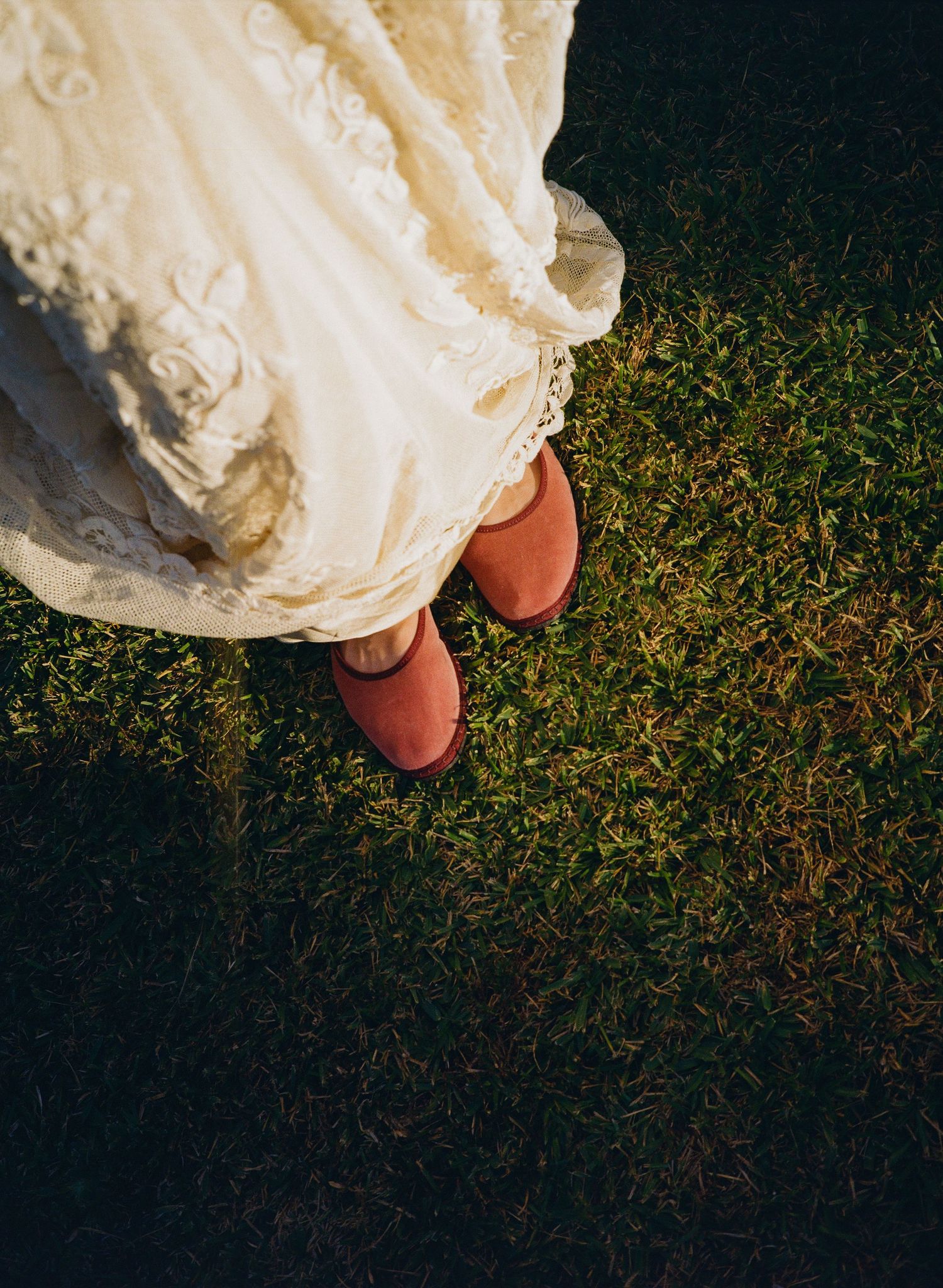 Close-up editorial detail shot of white wedding dress hem against green grass.