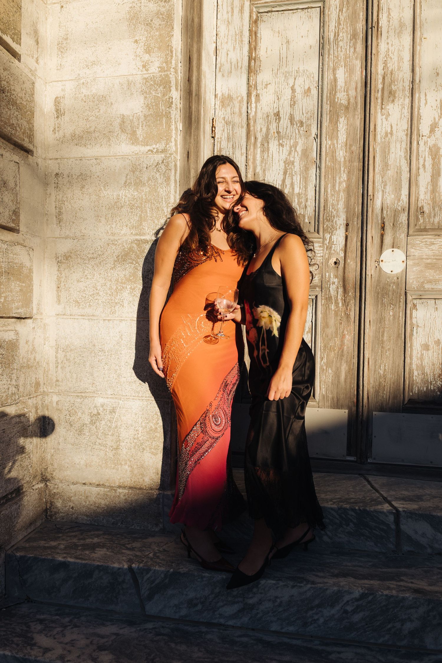 Two bridesmaids standing against the doors of the Marigny Opera House in New Orleans in golden sunlight.